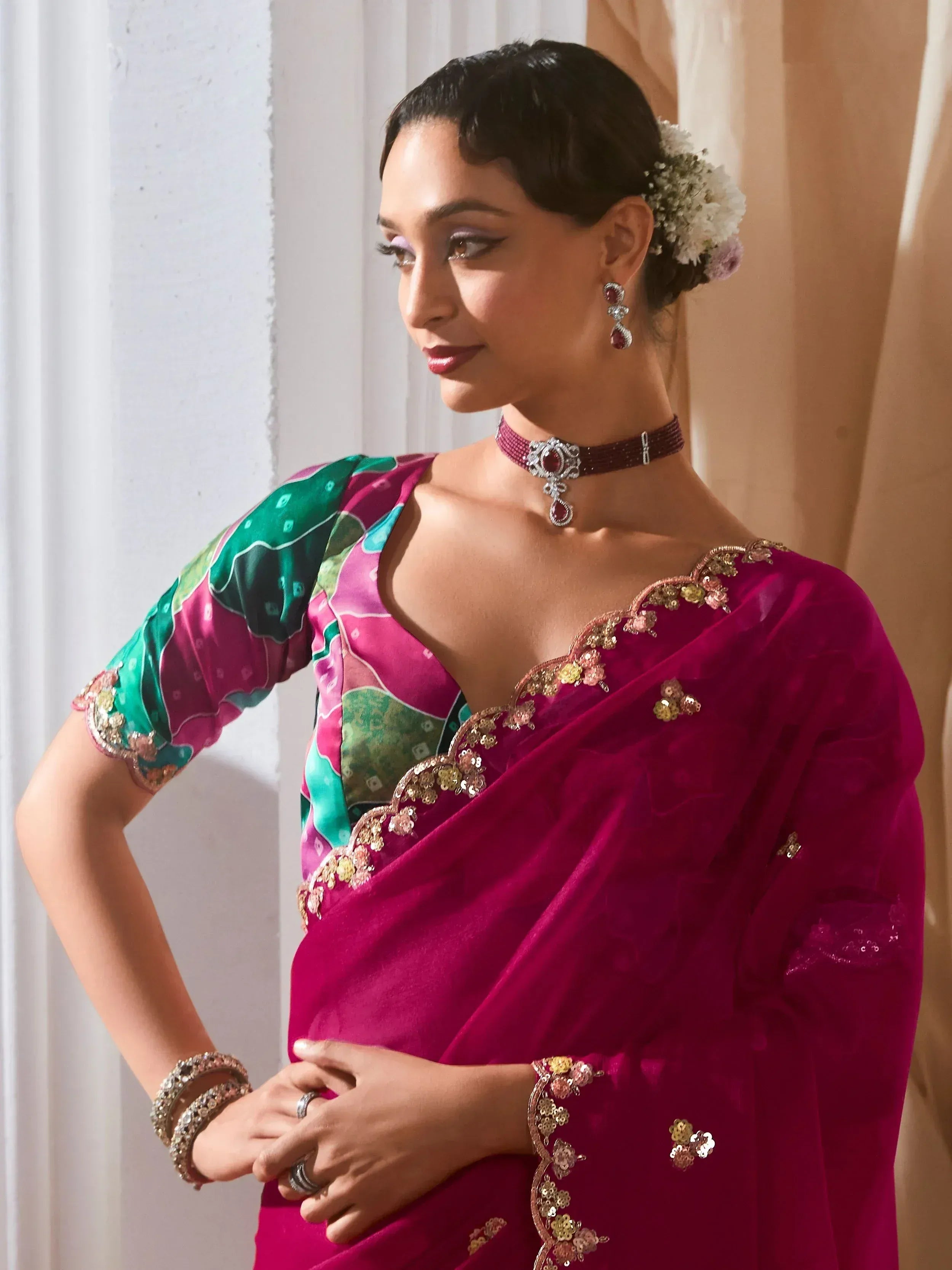 Woman in vibrant pink velvet saree with floral embroidery and green blouse, styled with jewelry for Indian ethnic wear
