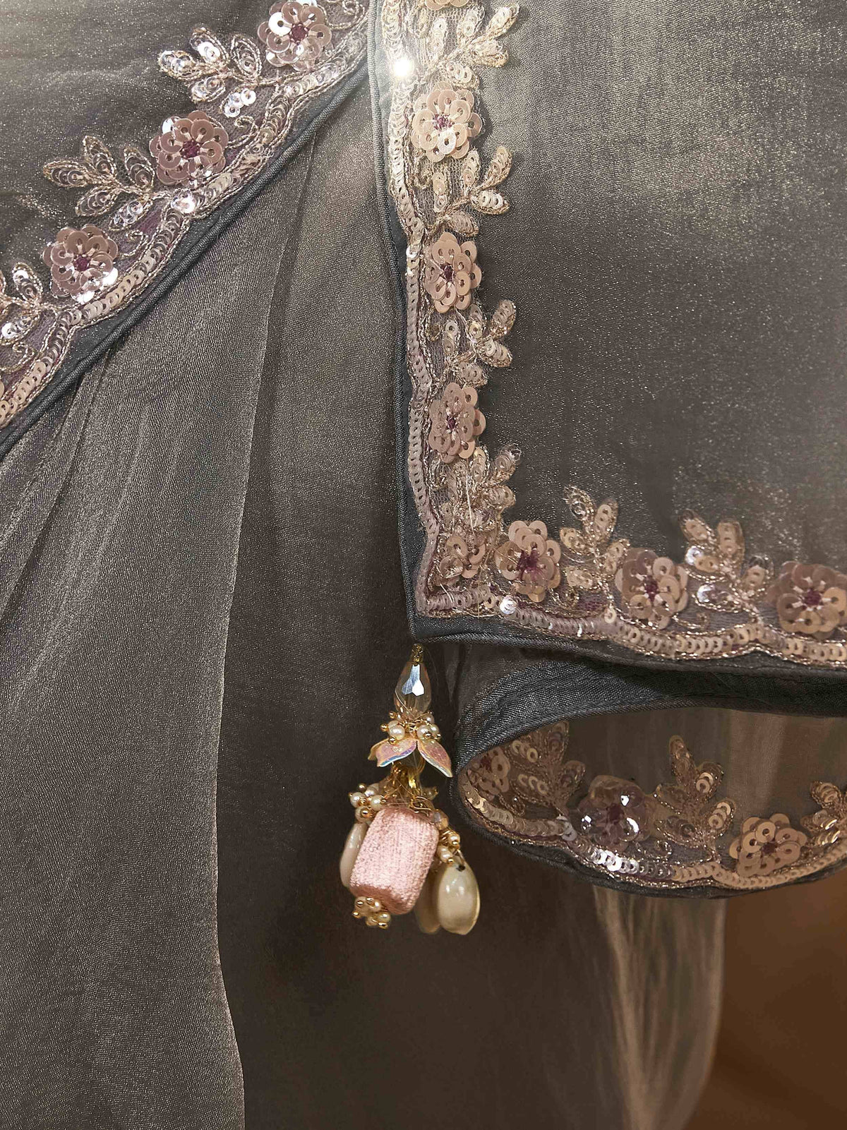 Elegant grey ethnic gown with gold sequin floral embroidery and dangling pearl tassels, perfect for Indian weddings.