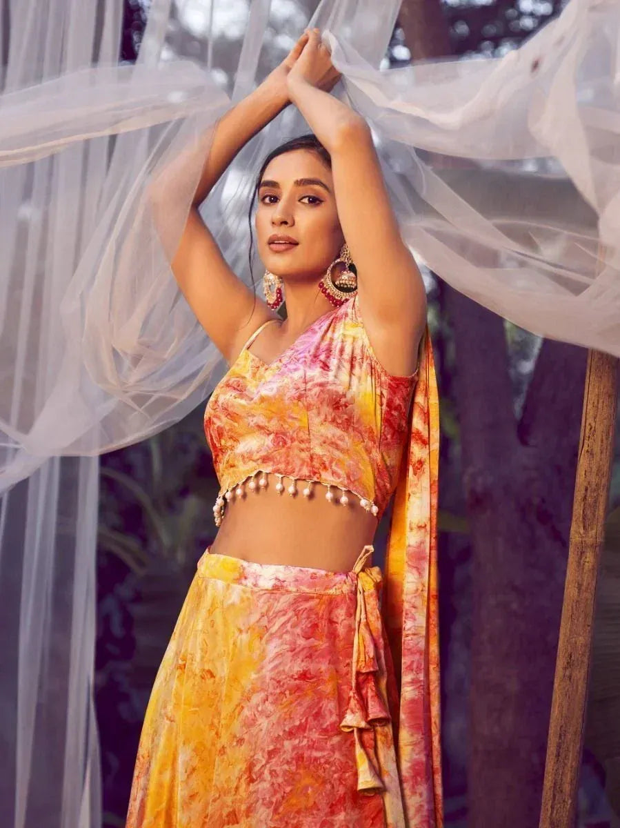 Woman in vibrant tie-dye lehenga choli with pearl embellishments, styled under sheer drapes for ethnic wear