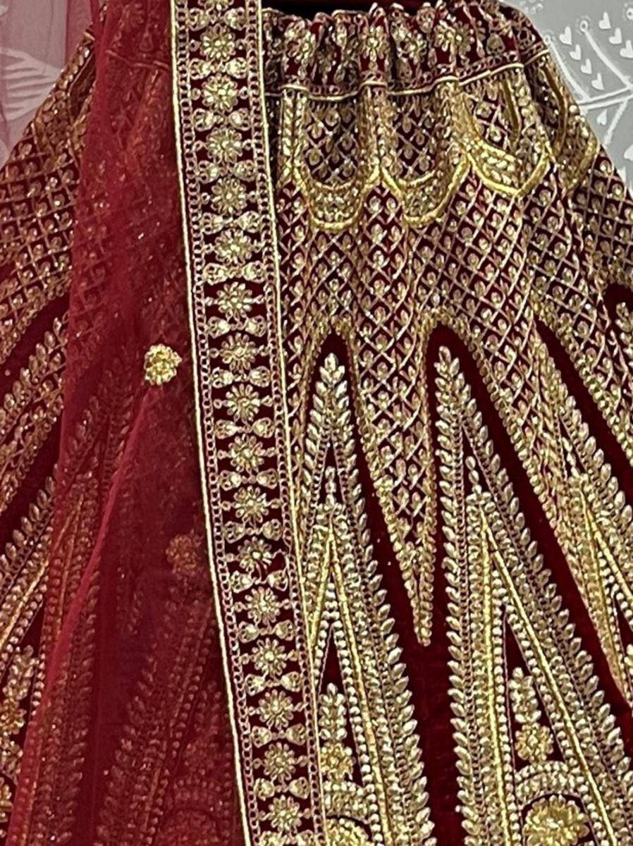 Rich maroon velvet lehenga with intricate gold embroidery and detailed border work, perfect for weddings.