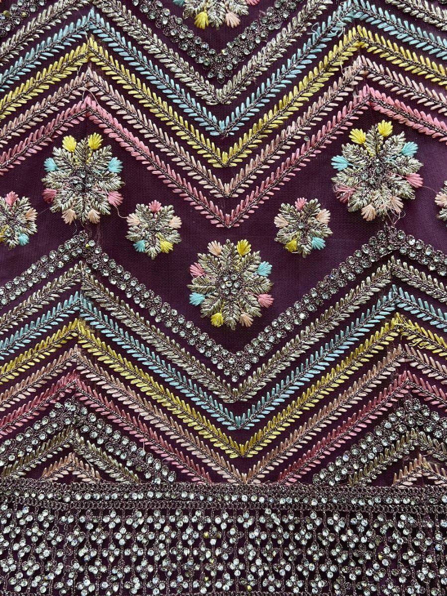 Embroidered ethnic wear with colorful threadwork, floral motifs, and crystal embellishments on deep purple fabric