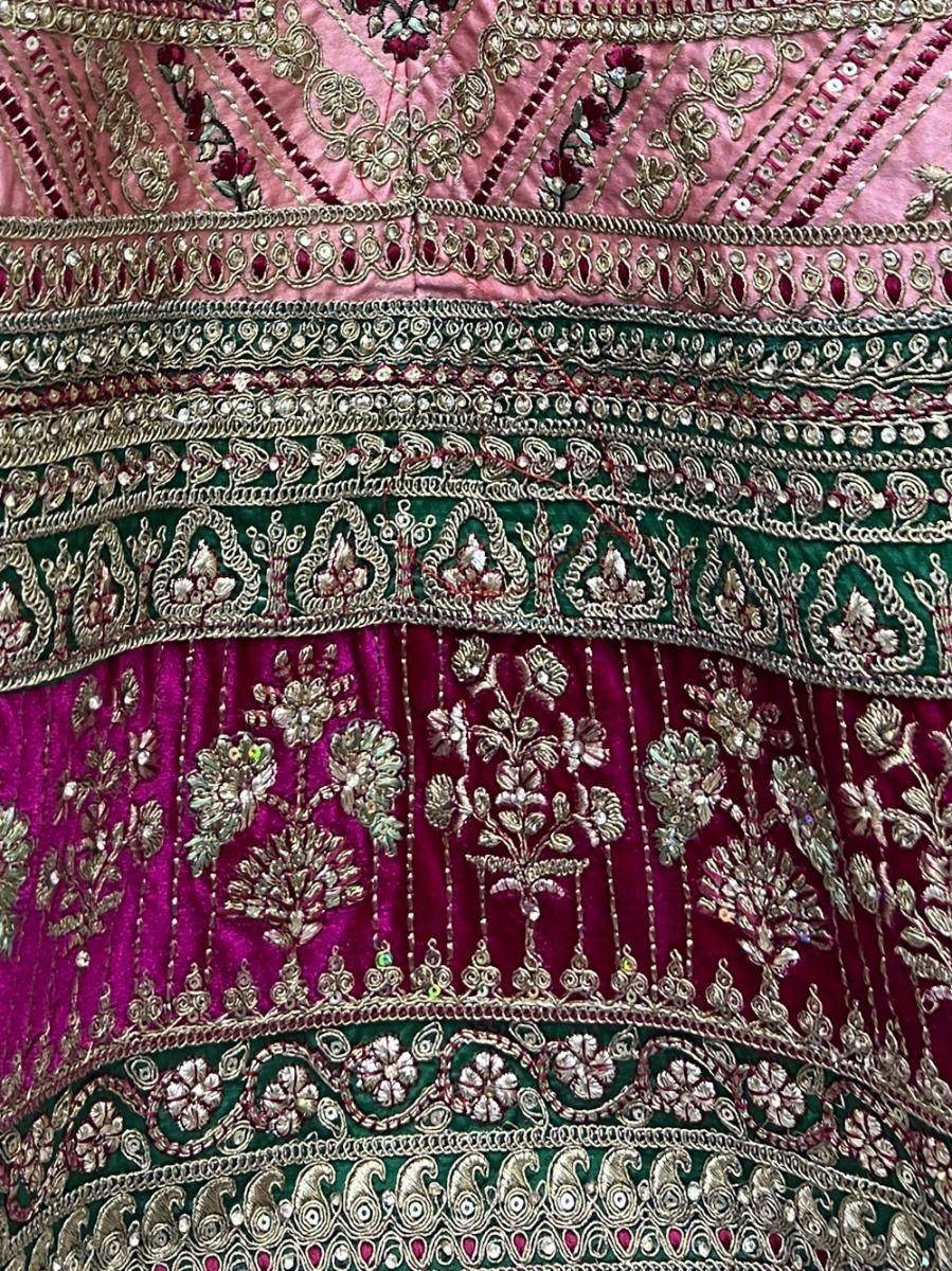 Luxury Indian lehenga with intricate gold embroidery, floral motifs, and velvet fabric in pink, green, and magenta hues.
