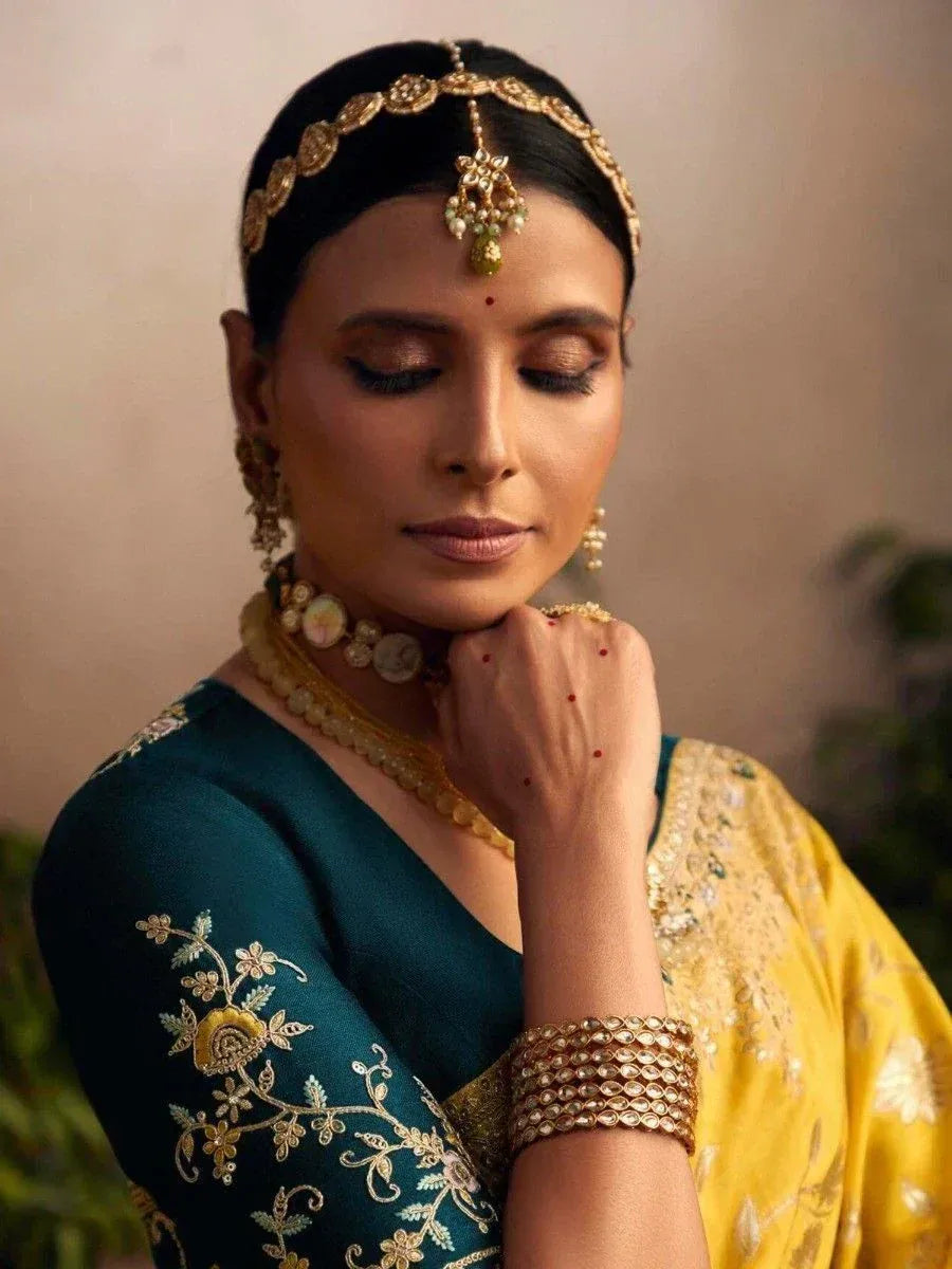 Woman in elegant teal and yellow embroidered saree with traditional gold jewelry and maang tikka