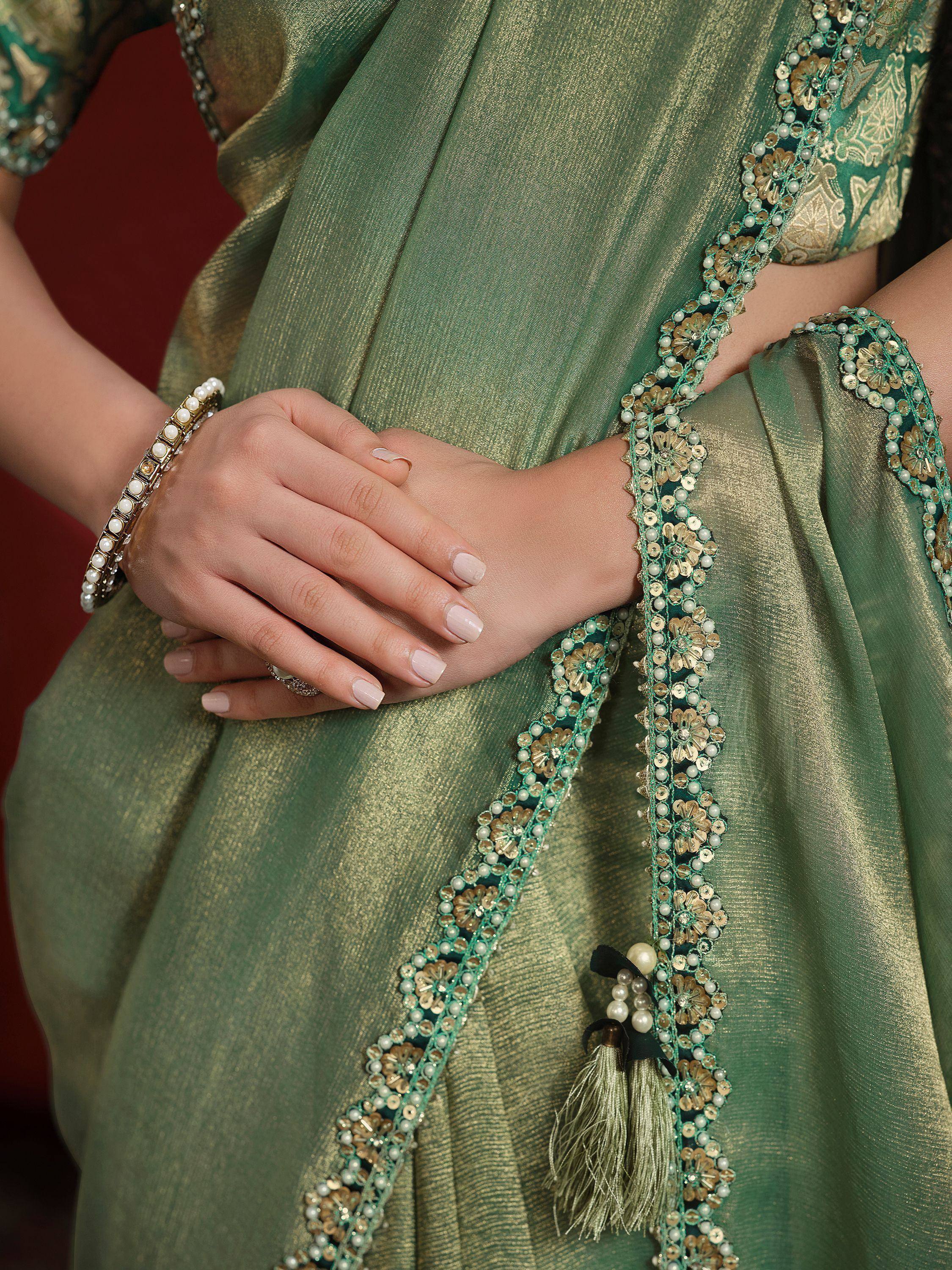 Green ethnic saree with gold embroidery, pearl beads, and tassels, paired with matching blouse and bangles.
