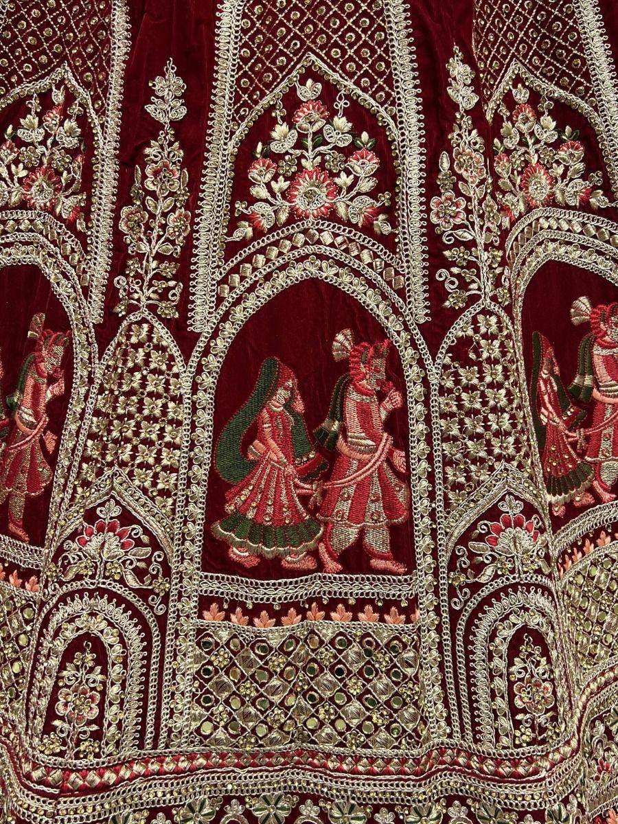 Richly embroidered maroon lehenga with gold floral motifs and traditional couple scenes