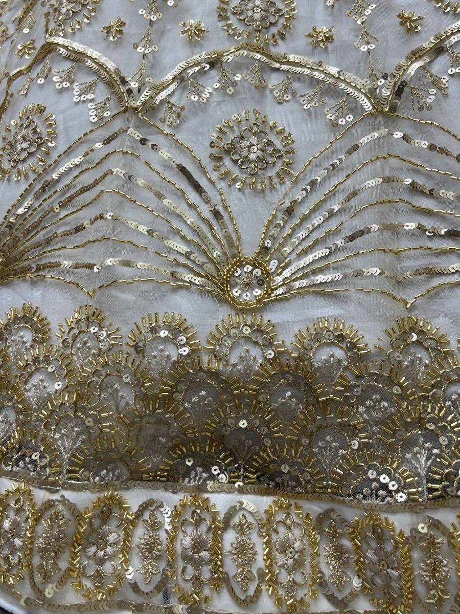 Gold and silver sequin embroidery on white ethnic wear fabric, featuring floral and fan patterns for lehenga or saree.