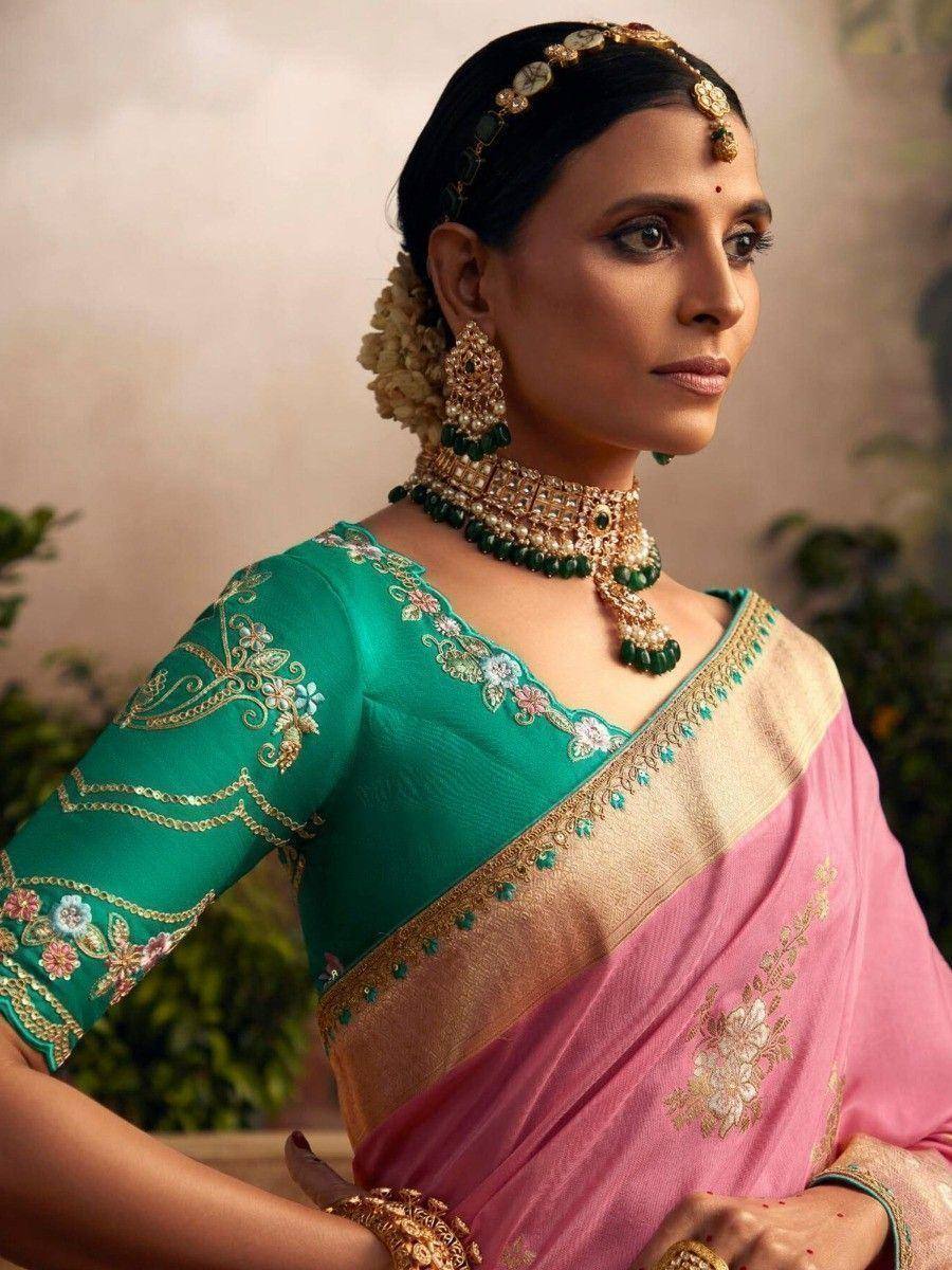 Elegant woman in pink and green embroidered saree with gold jewelry, perfect for Indian ethnic occasions.