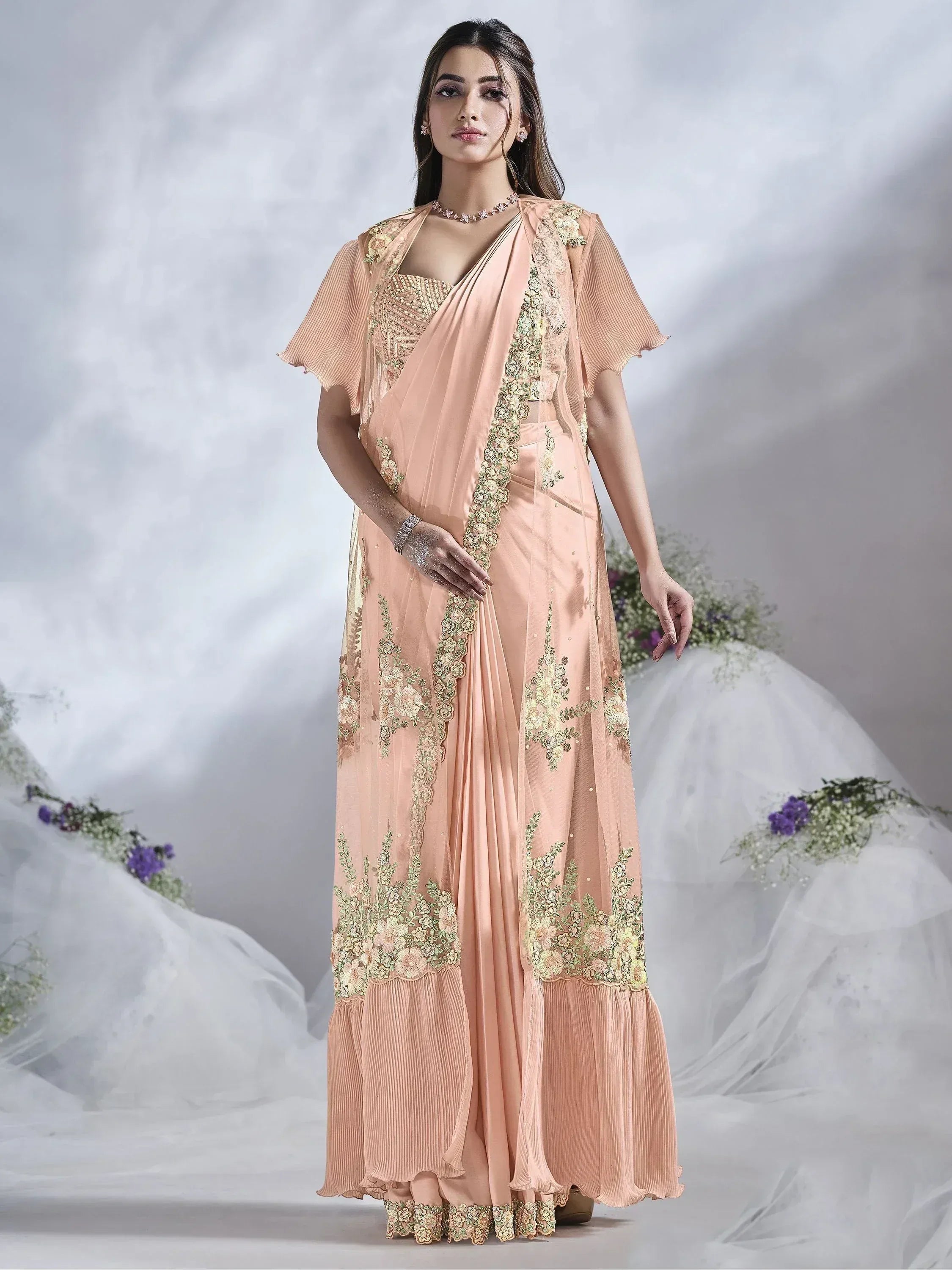 Elegant peach saree with golden floral embroidery and pleated hem, perfect for Indian ethnic wear.