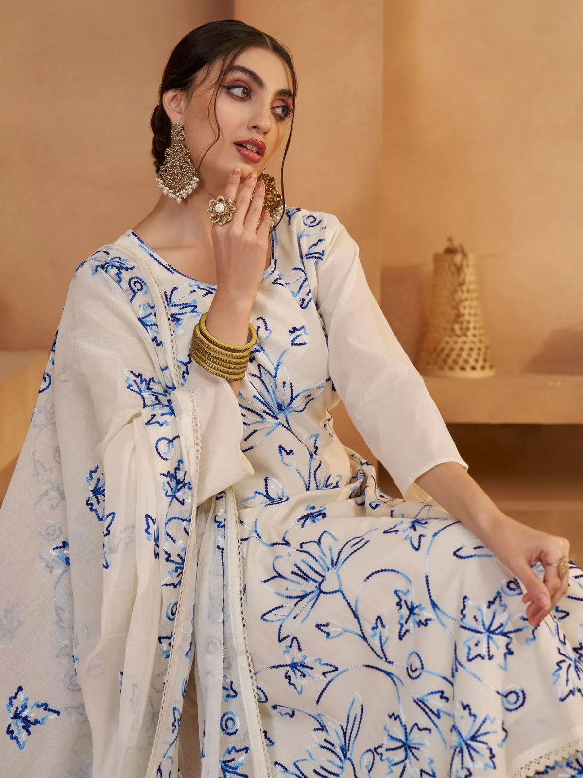 White ethnic salwar kameez with blue floral embroidery, paired with gold jewelry for festive occasions.