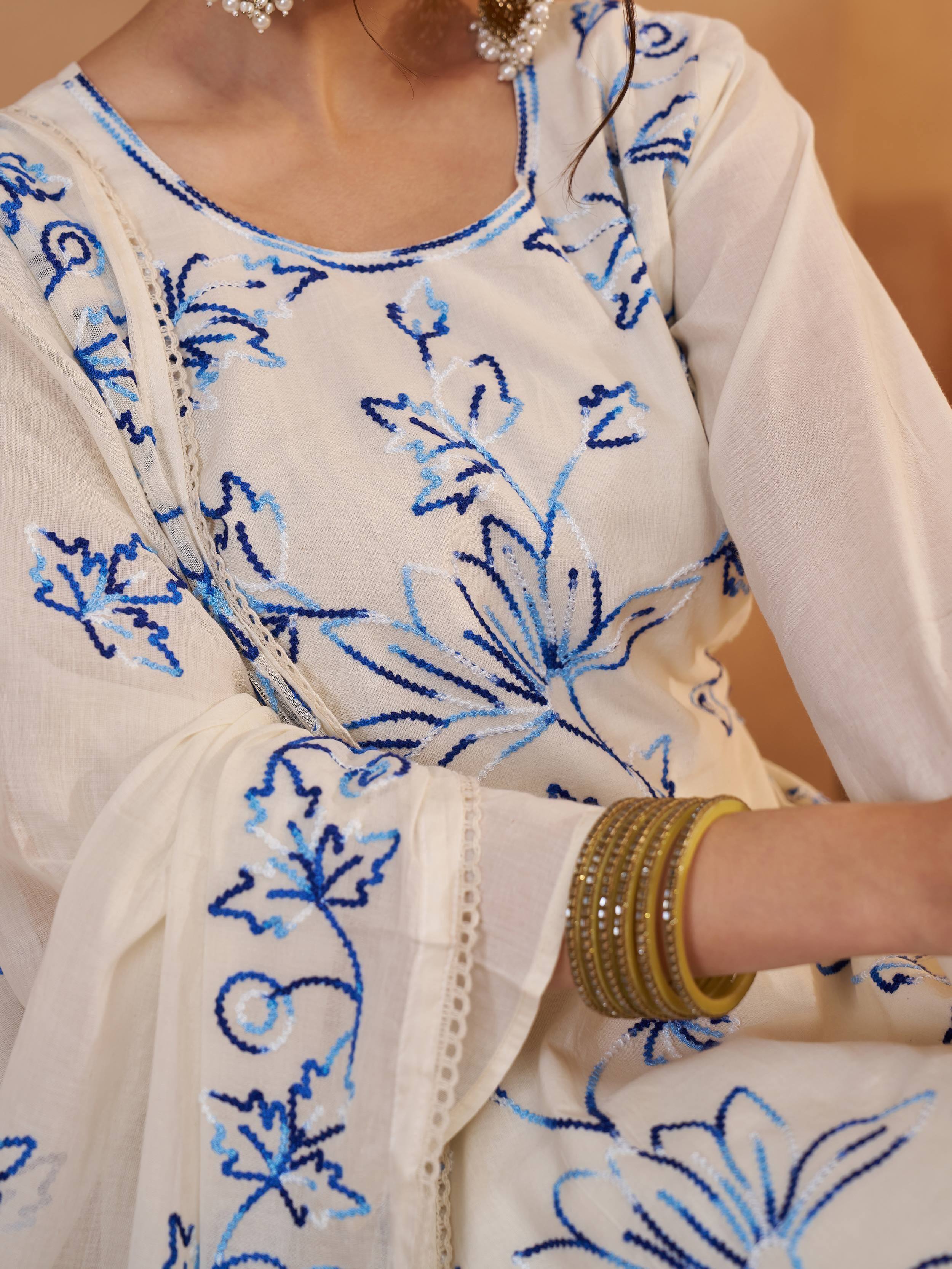 Cream ethnic kurta with blue floral embroidery, lace detailing, and gold bangles