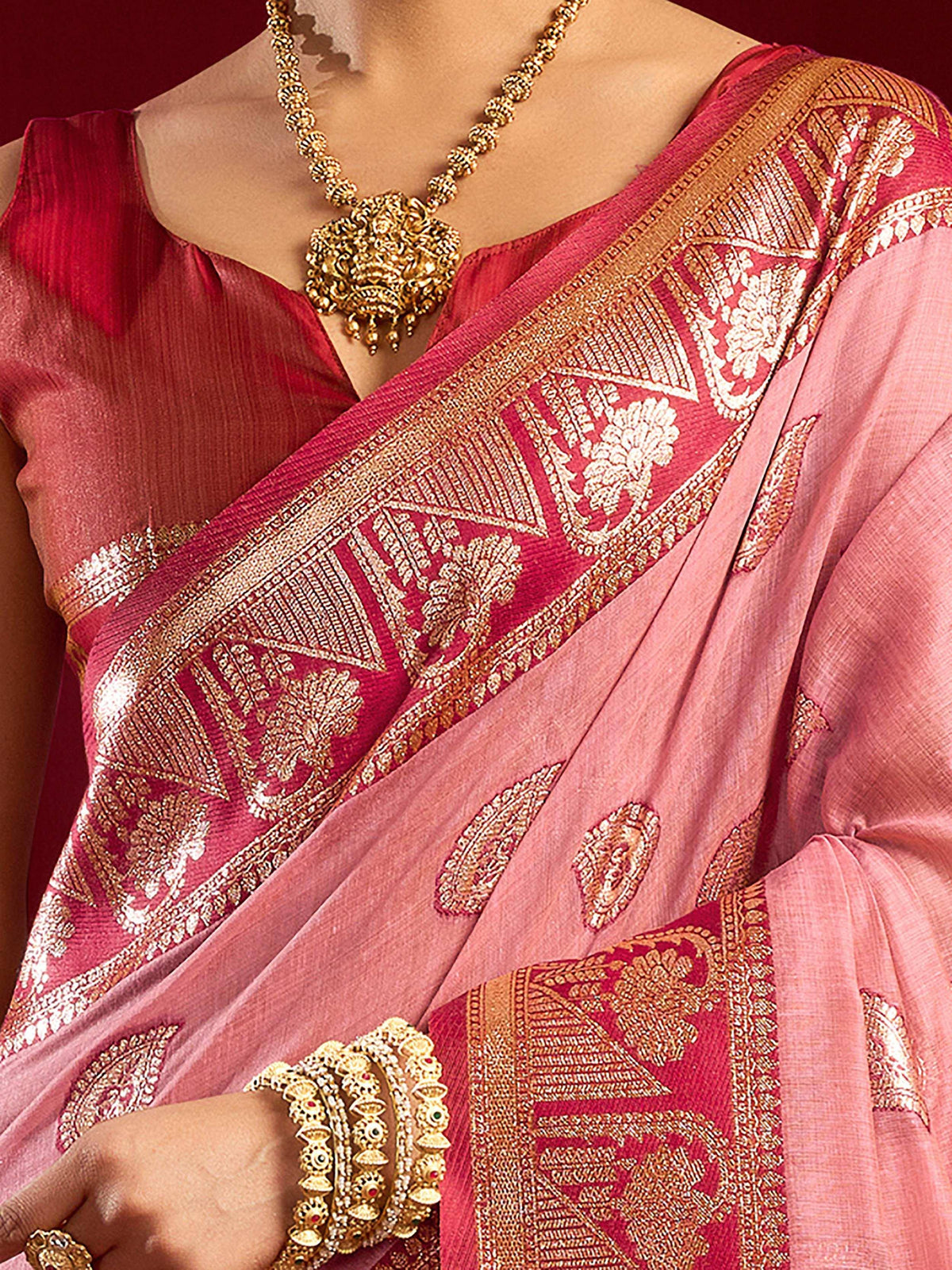 Pink and red designer saree with gold zari work, paired with traditional gold jewelry for ethnic wear.