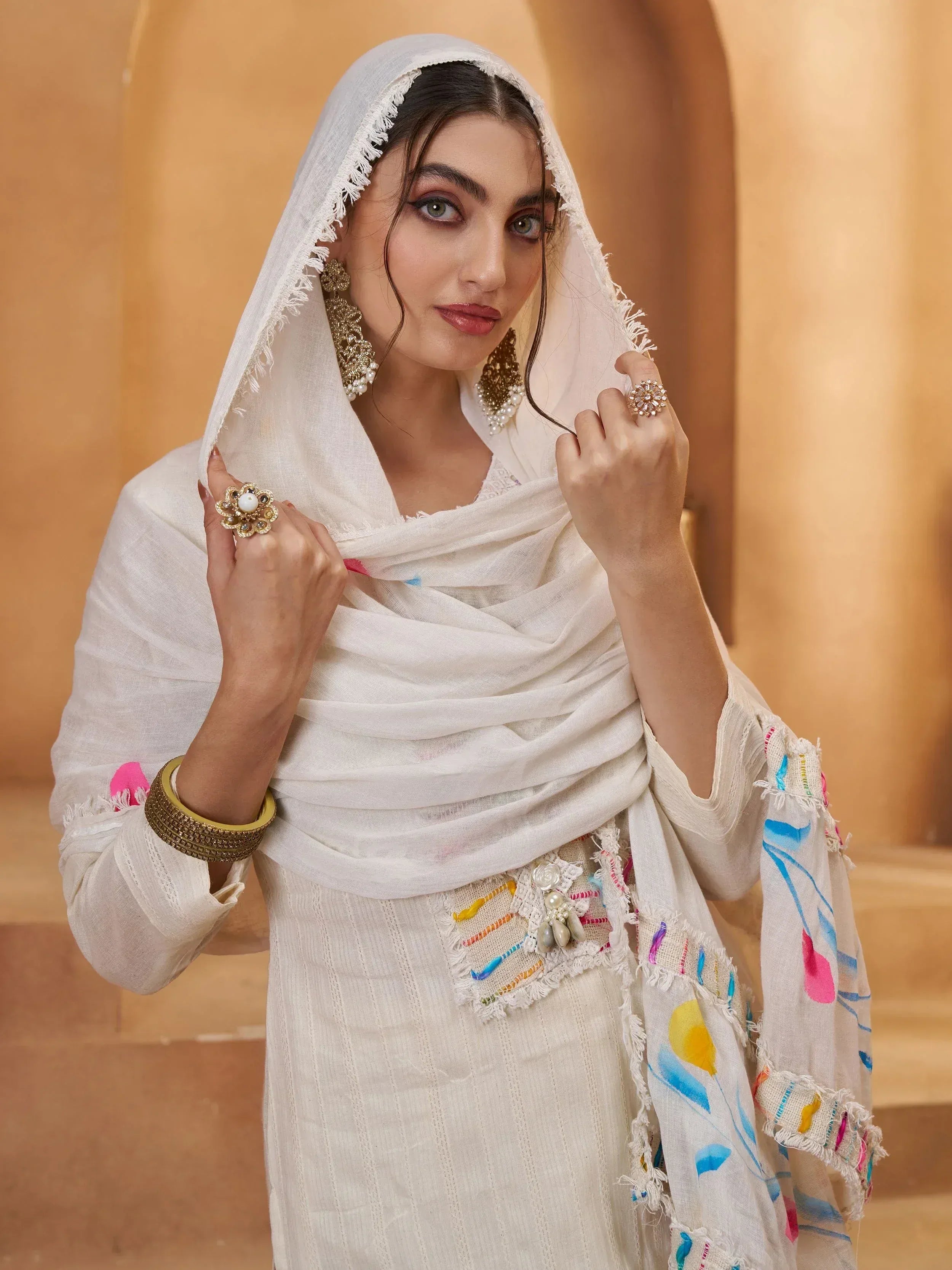 White ethnic salwar kameez with colorful embroidery, fringe dupatta, and statement jewelry for Indian wear