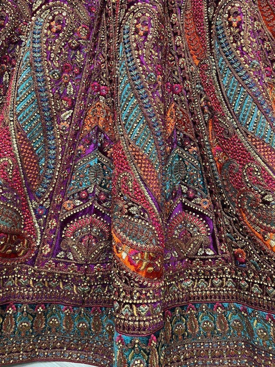 Richly embroidered Indian lehenga with vibrant paisley and floral motifs in purple, teal, and gold.