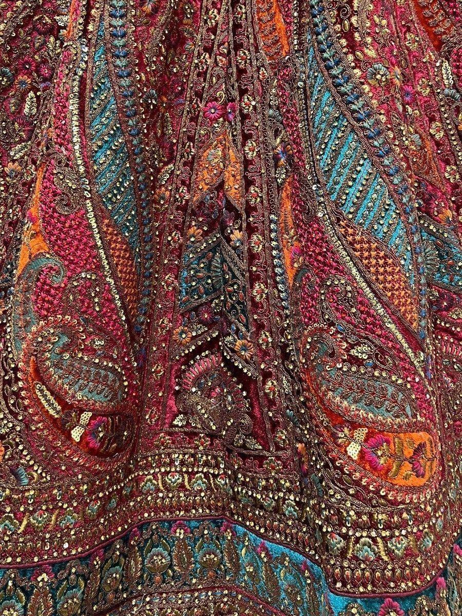 Richly embroidered Indian ethnic lehenga with paisley and floral motifs in maroon, teal, and gold.