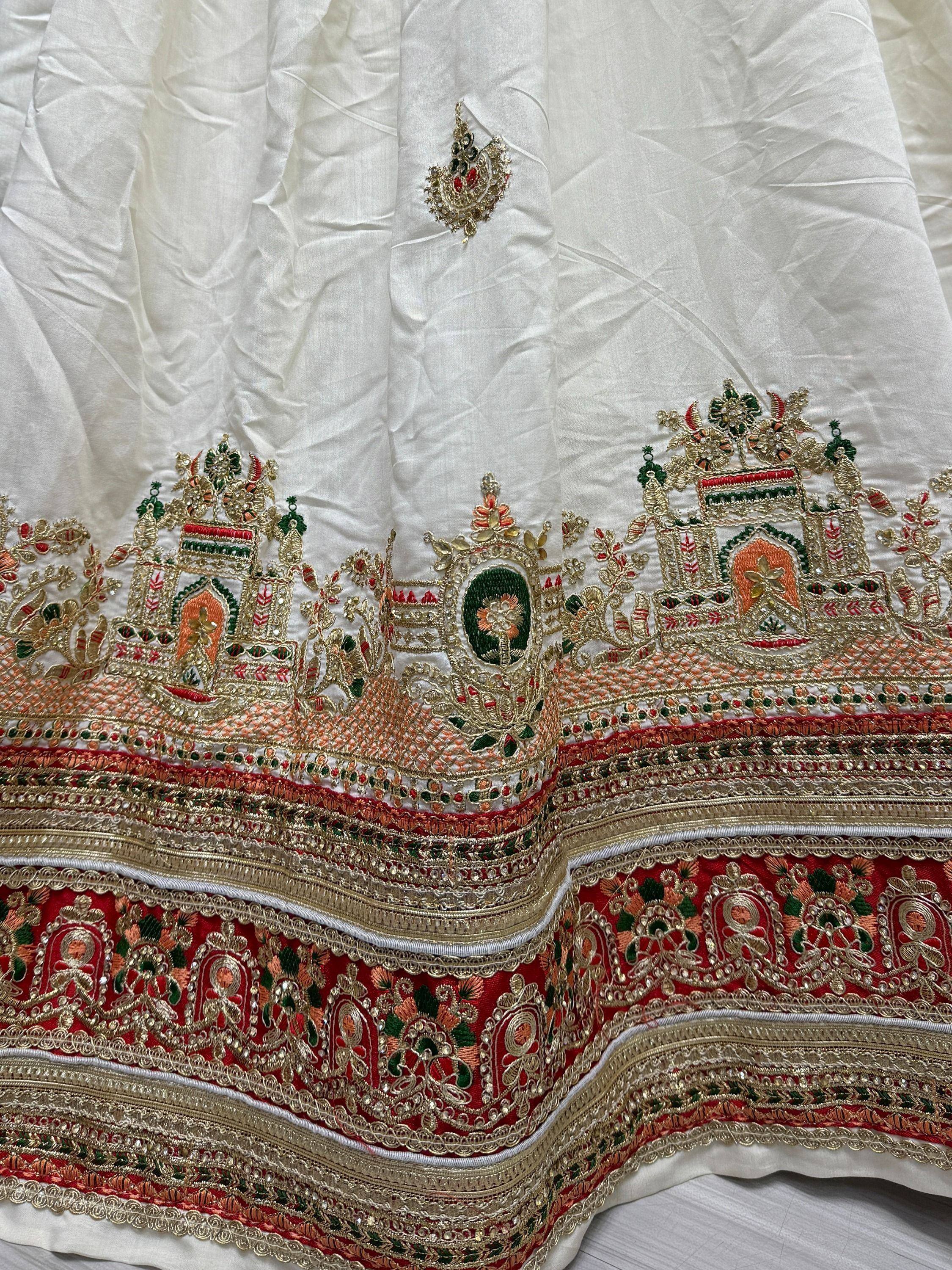 White lehenga with intricate gold, red, and green temple embroidery and detailed border work