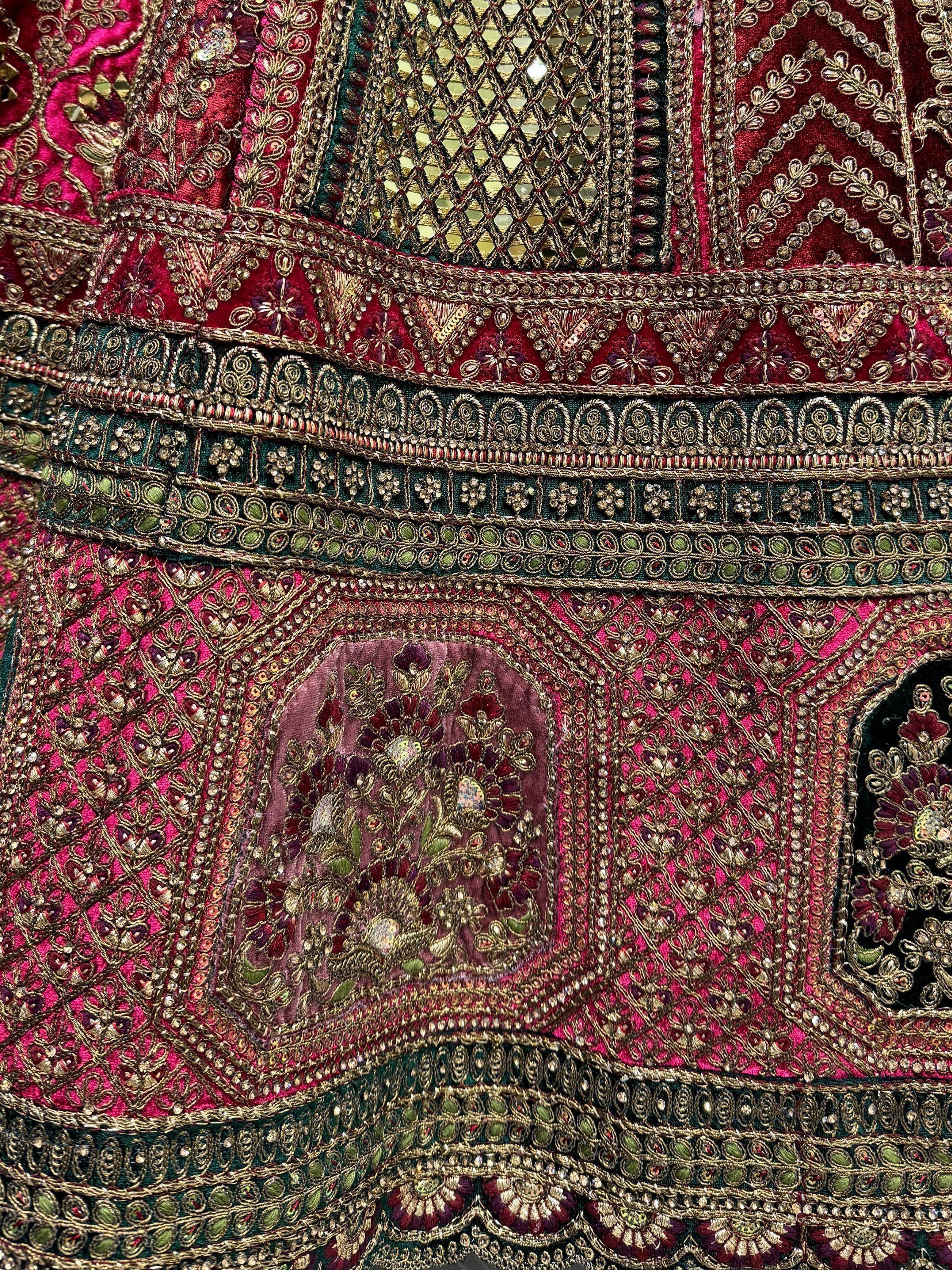 Luxury Indian ethnic wear with intricate gold embroidery, mirror work, and vibrant pink and maroon velvet fabric details.