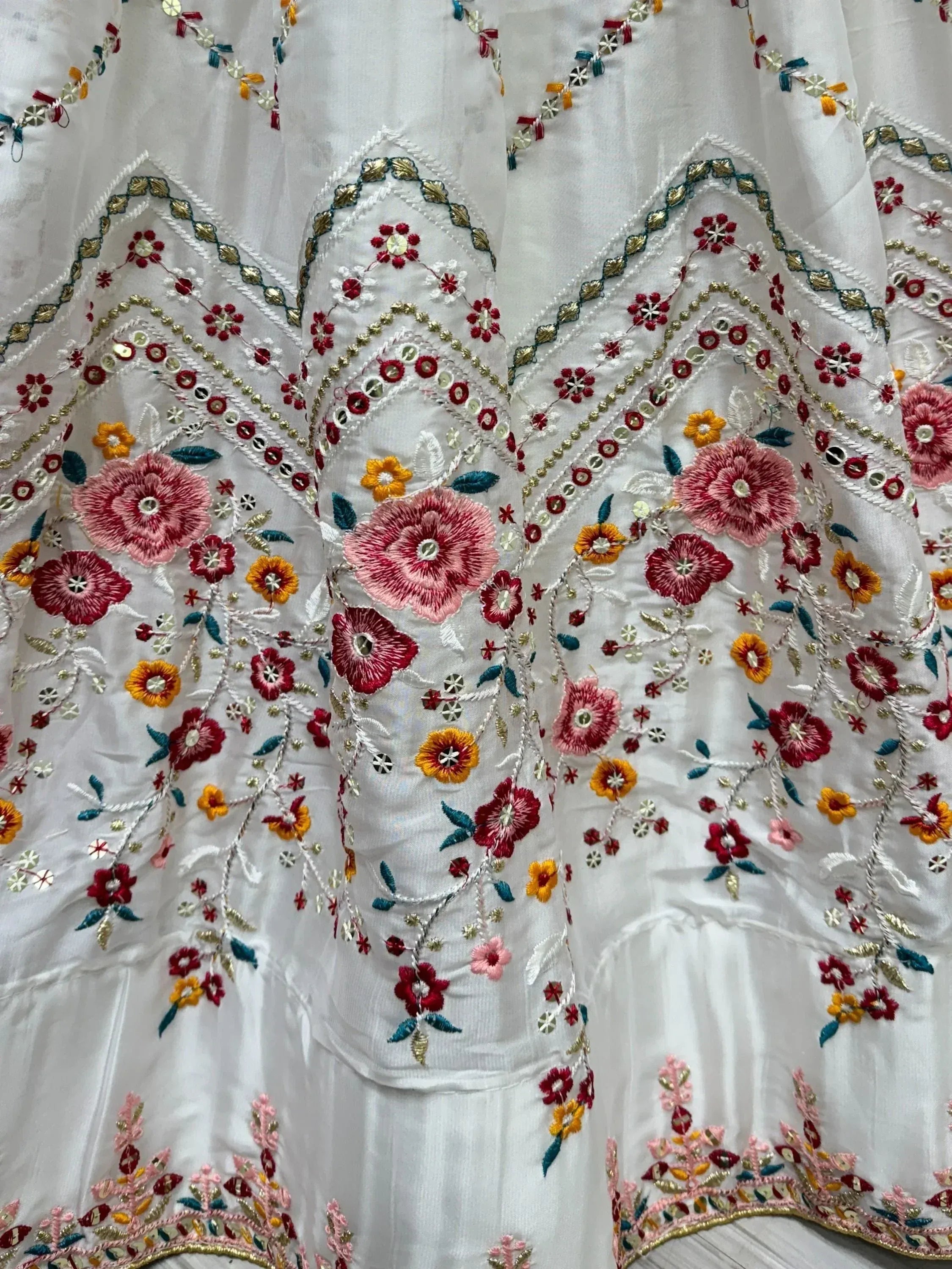 White ethnic gown with vibrant floral embroidery and mirror work, perfect for Indian occasions.