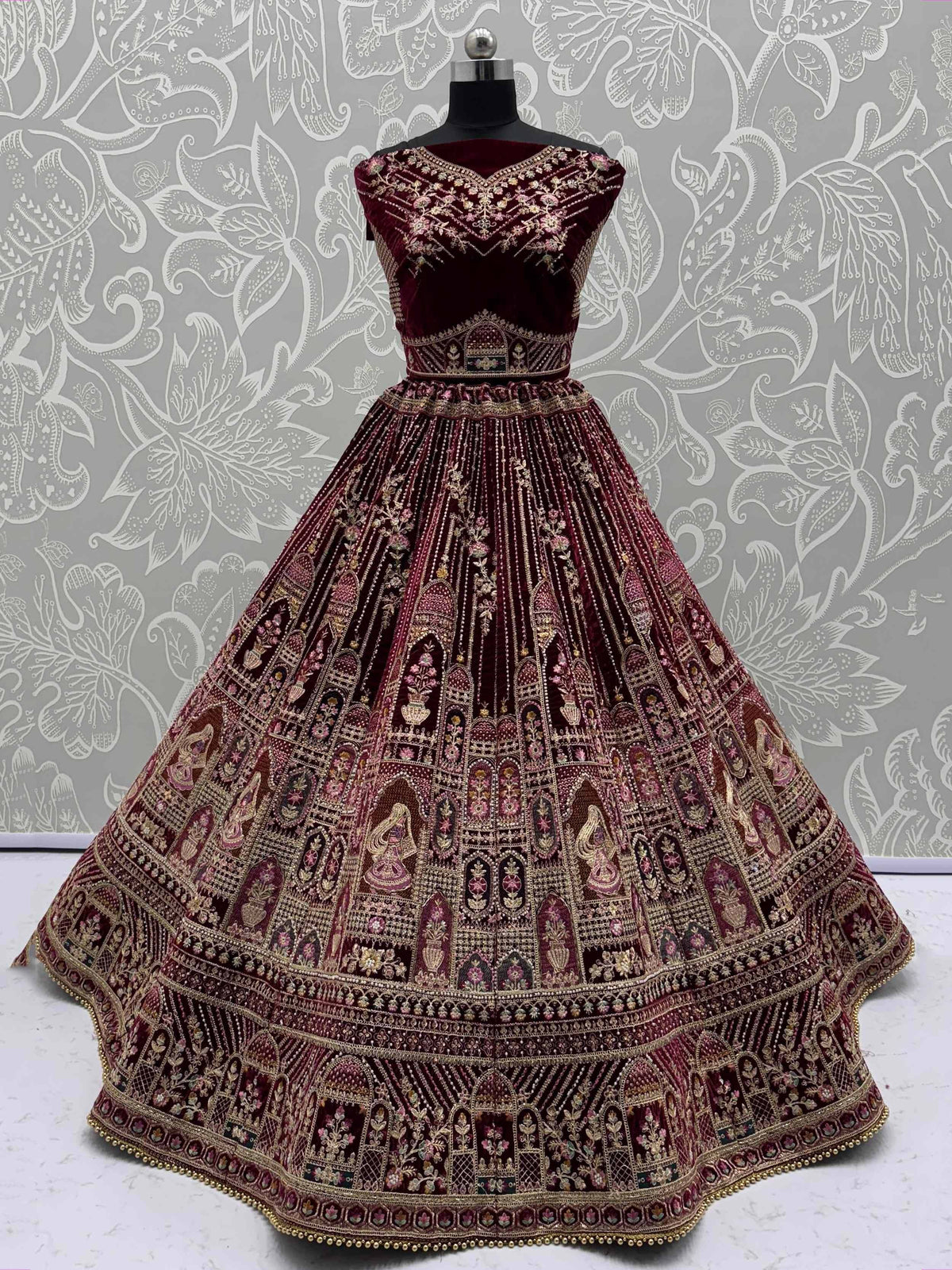Maroon velvet designer lehenga choli with heavy gold embroidery and floral motifs, perfect for weddings.