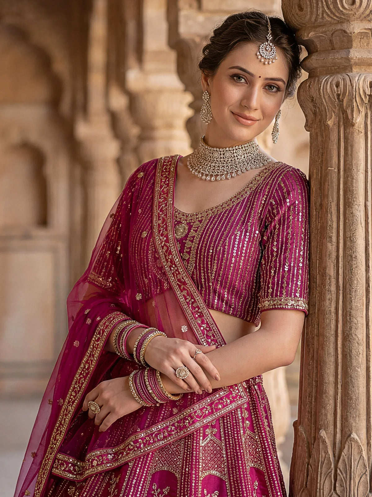 Woman wearing a magenta designer lehenga choli with silver embroidery and traditional jewelry.