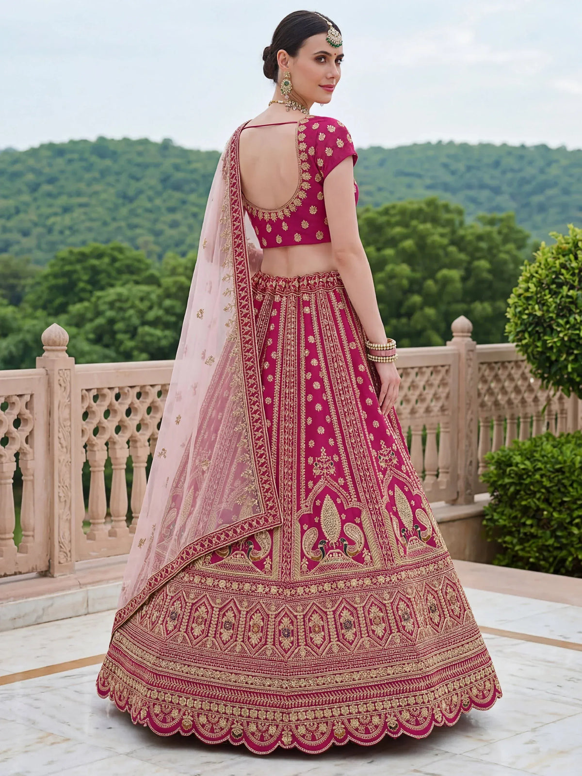 Woman in a magenta designer lehenga choli with gold embroidery and a sheer pink dupatta.