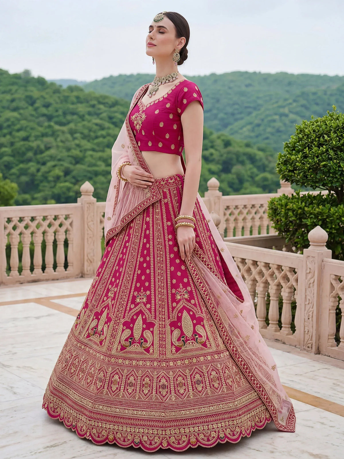 Woman wearing a magenta designer lehenga choli with gold embroidery and a pink dupatta