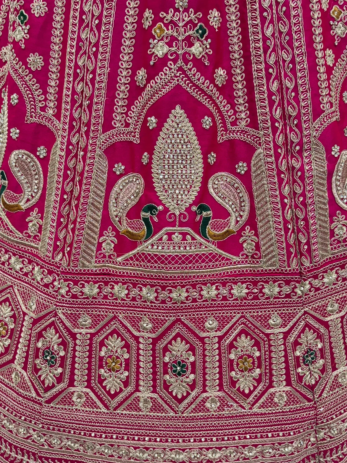 Close-up of pink ethnic lehenga fabric with gold embroidery and peacock motifs