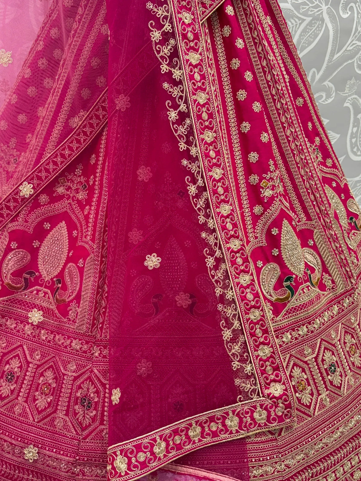 Close-up of a magenta designer lehenga with intricate gold zari embroidery and peacock motifs.