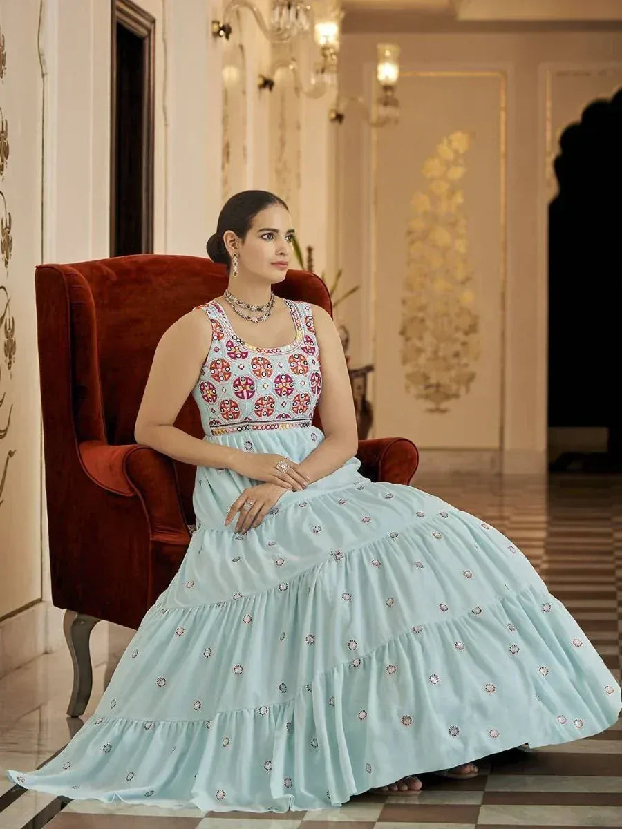Woman in light blue embroidered ethnic gown with tiered skirt, seated on red velvet chair