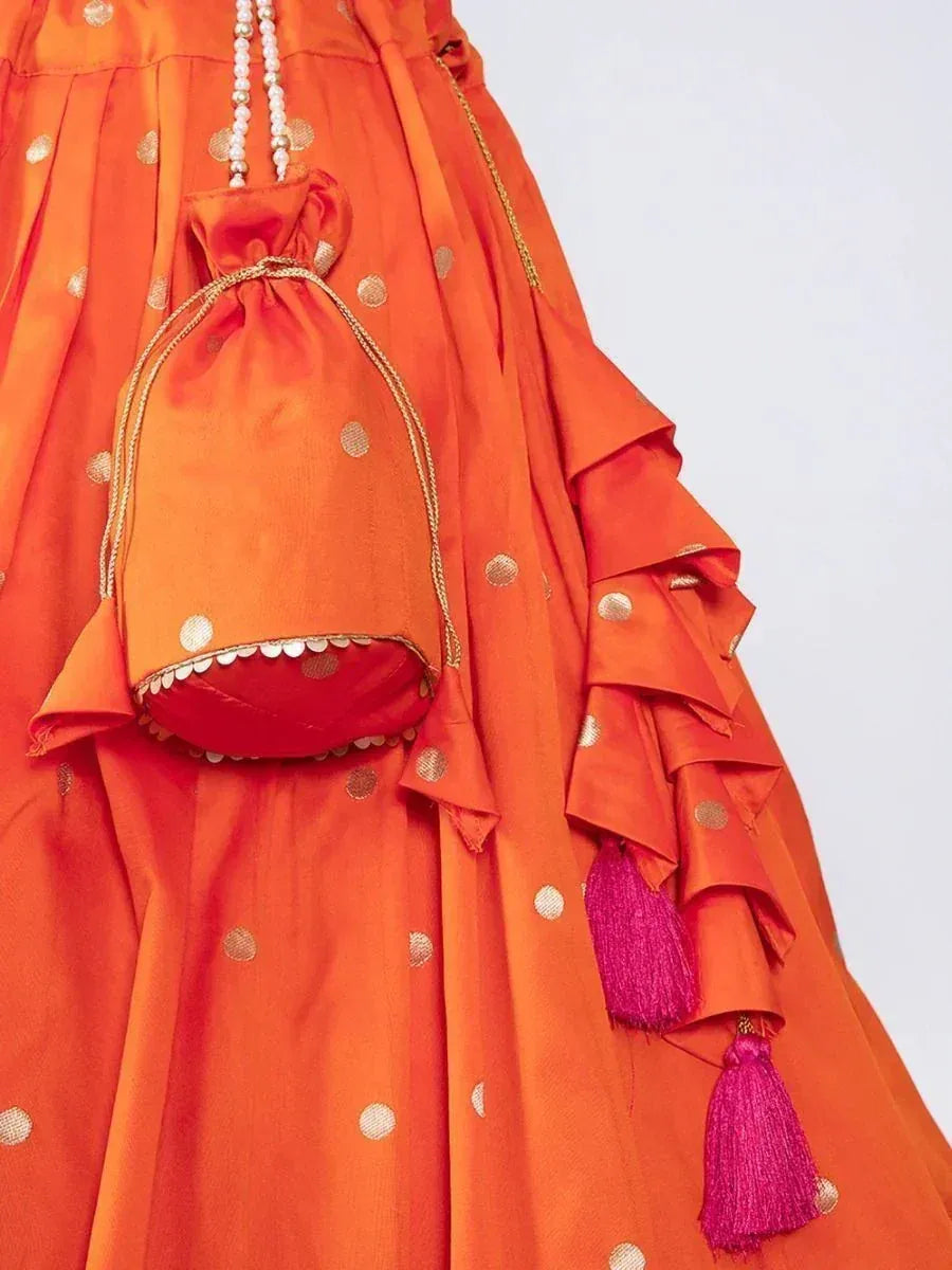 Orange ethnic lehenga with gold polka dots, ruffles, and pink tassels, paired with matching potli bag