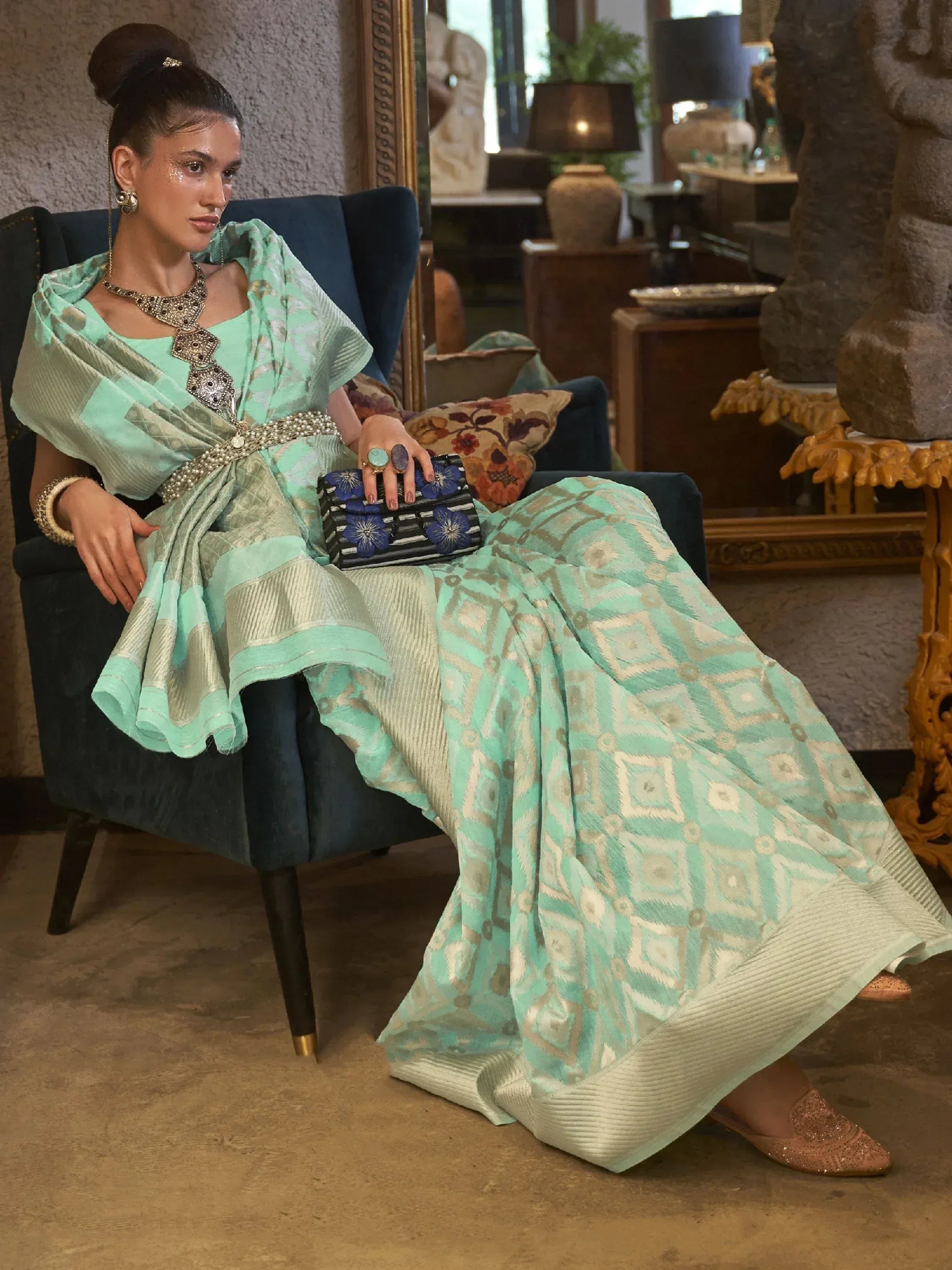 Mint green ethnic gown with geometric print, paired with statement jewelry and floral clutch, perfect for festive occasions.