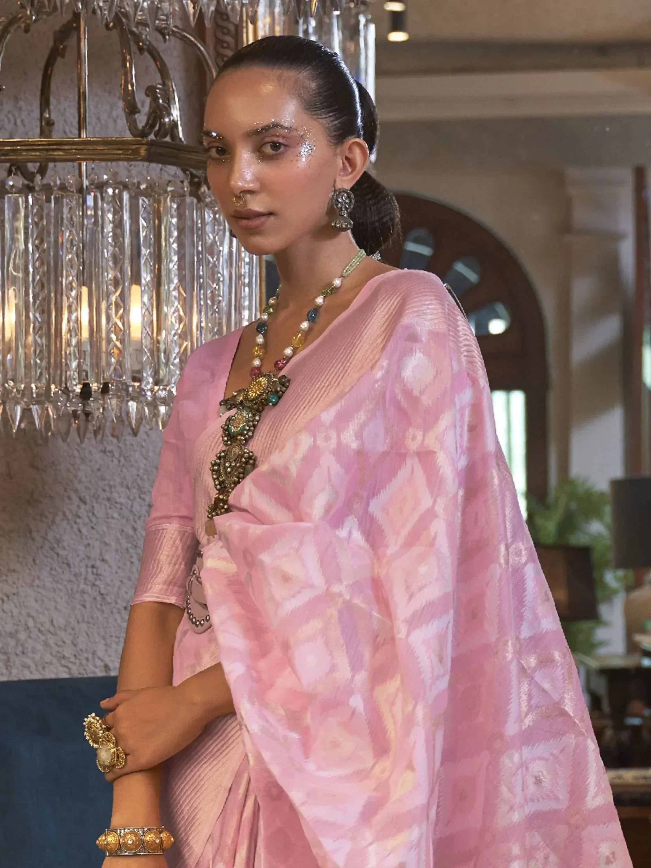 Pink designer saree with ikat pattern, ethnic jewelry, and festive makeup for Indian occasions