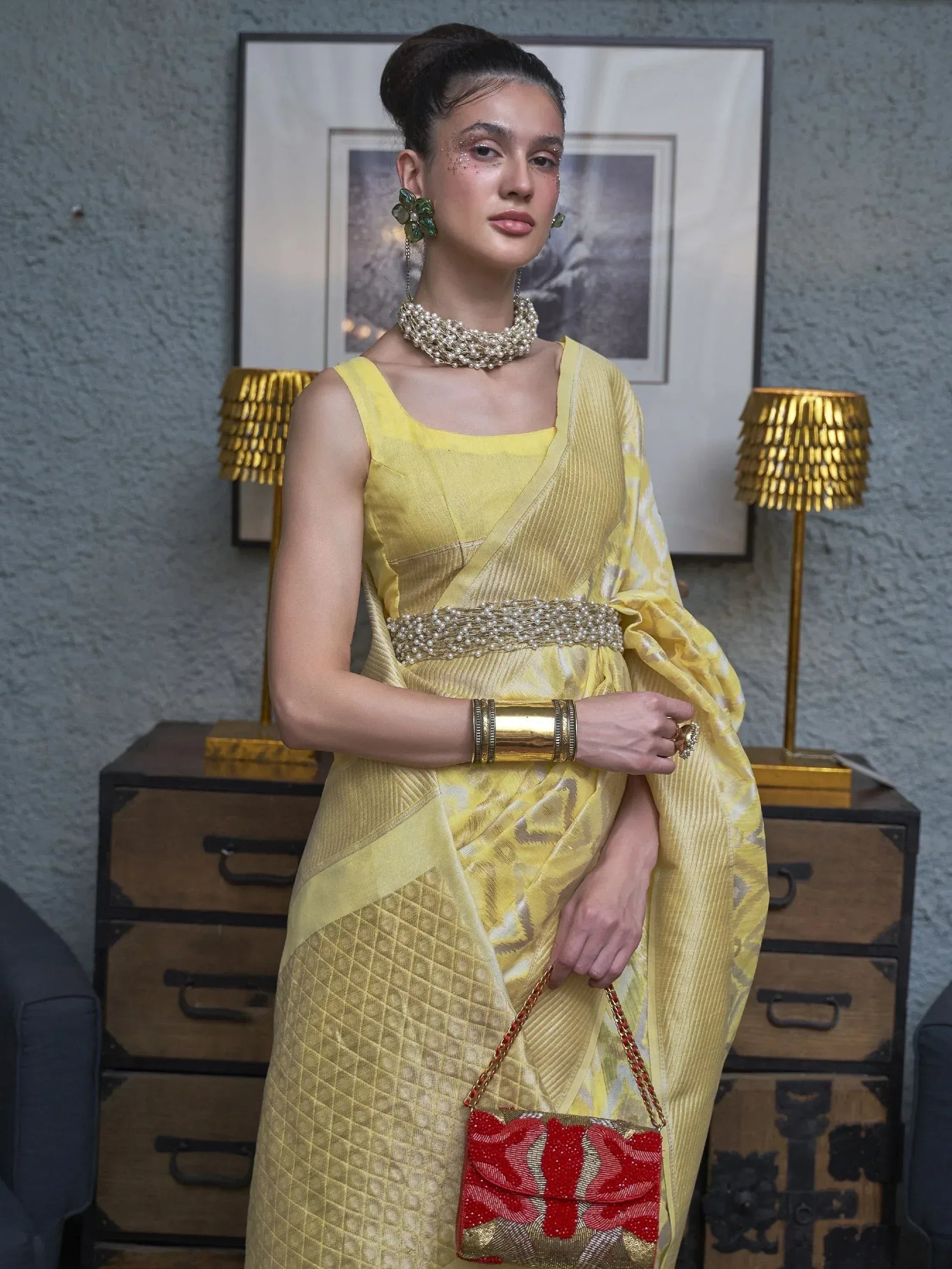 Yellow designer saree with pearl belt, gold jewelry, and red embellished clutch for ethnic wear