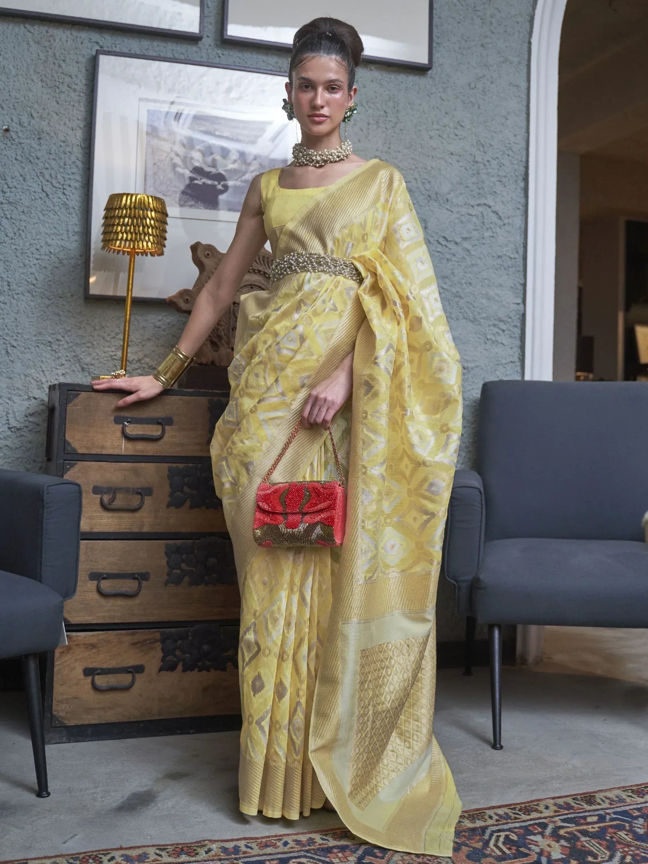 Yellow designer saree with geometric print, paired with statement jewelry and red clutch, perfect for ethnic occasions