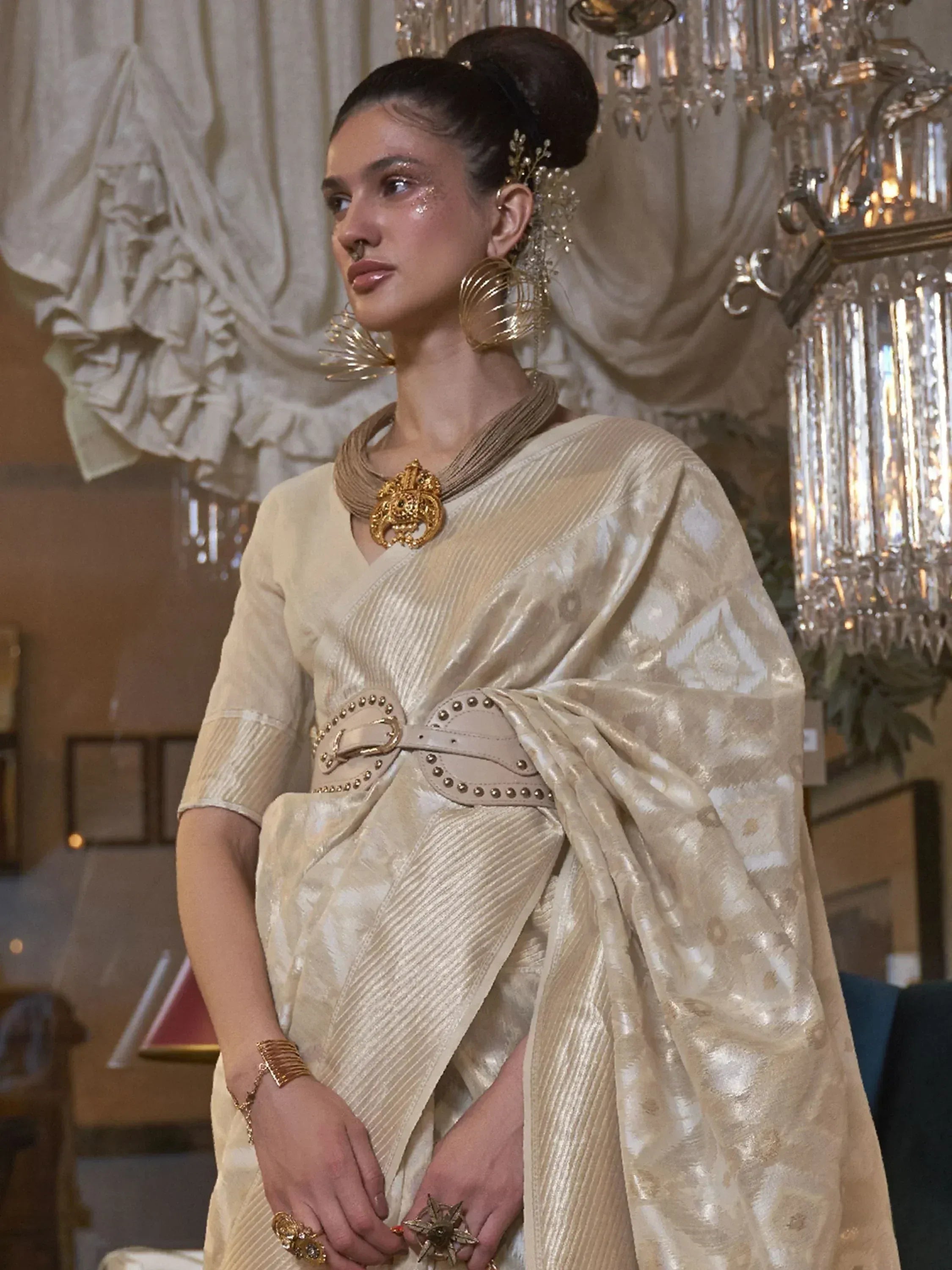 Elegant cream ethnic saree with gold jewelry and statement belt, perfect for Indian weddings or festive occasions.
