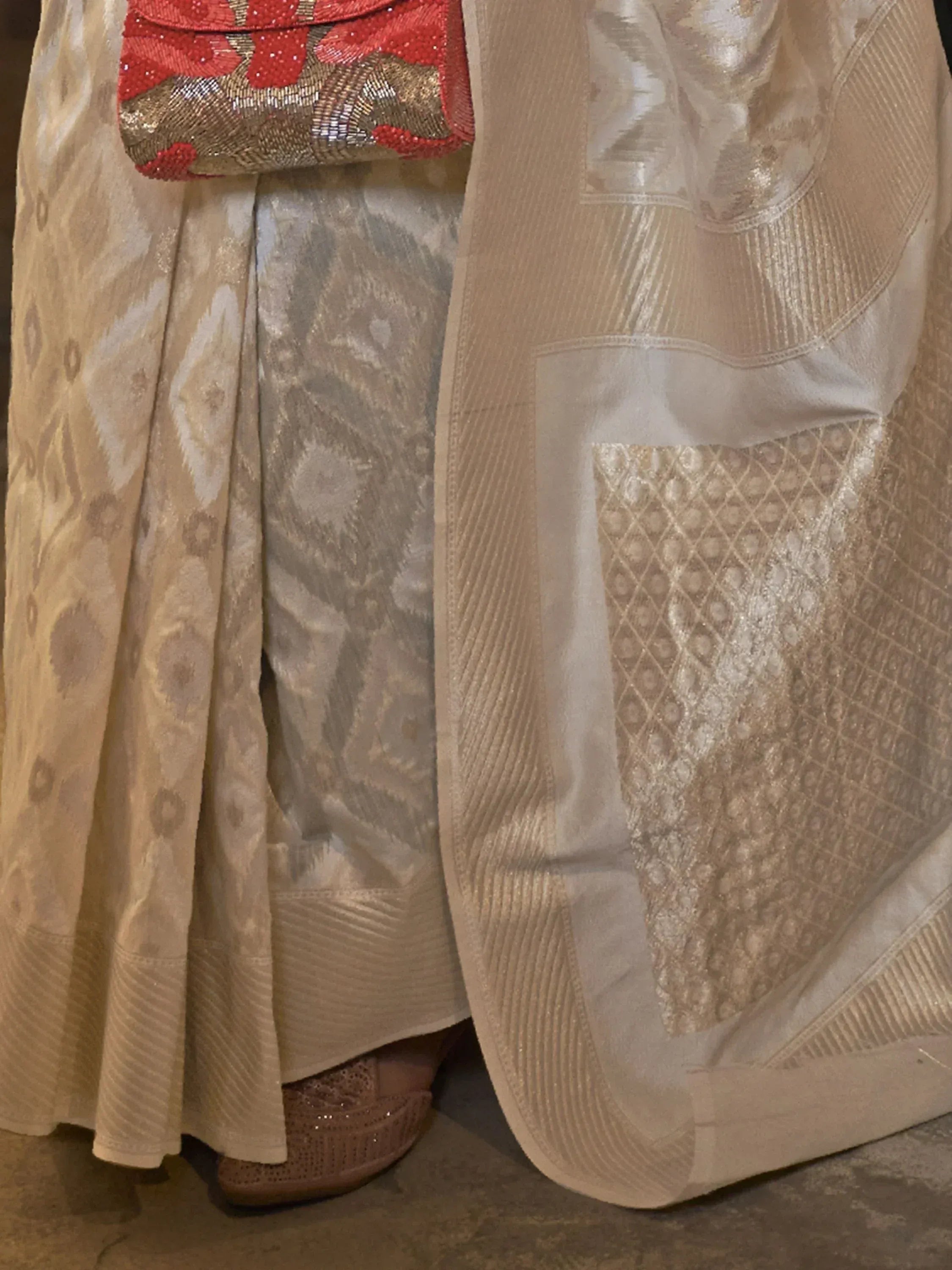 Beige ethnic gown with intricate patterns, paired with red sequin clutch and matching heels.