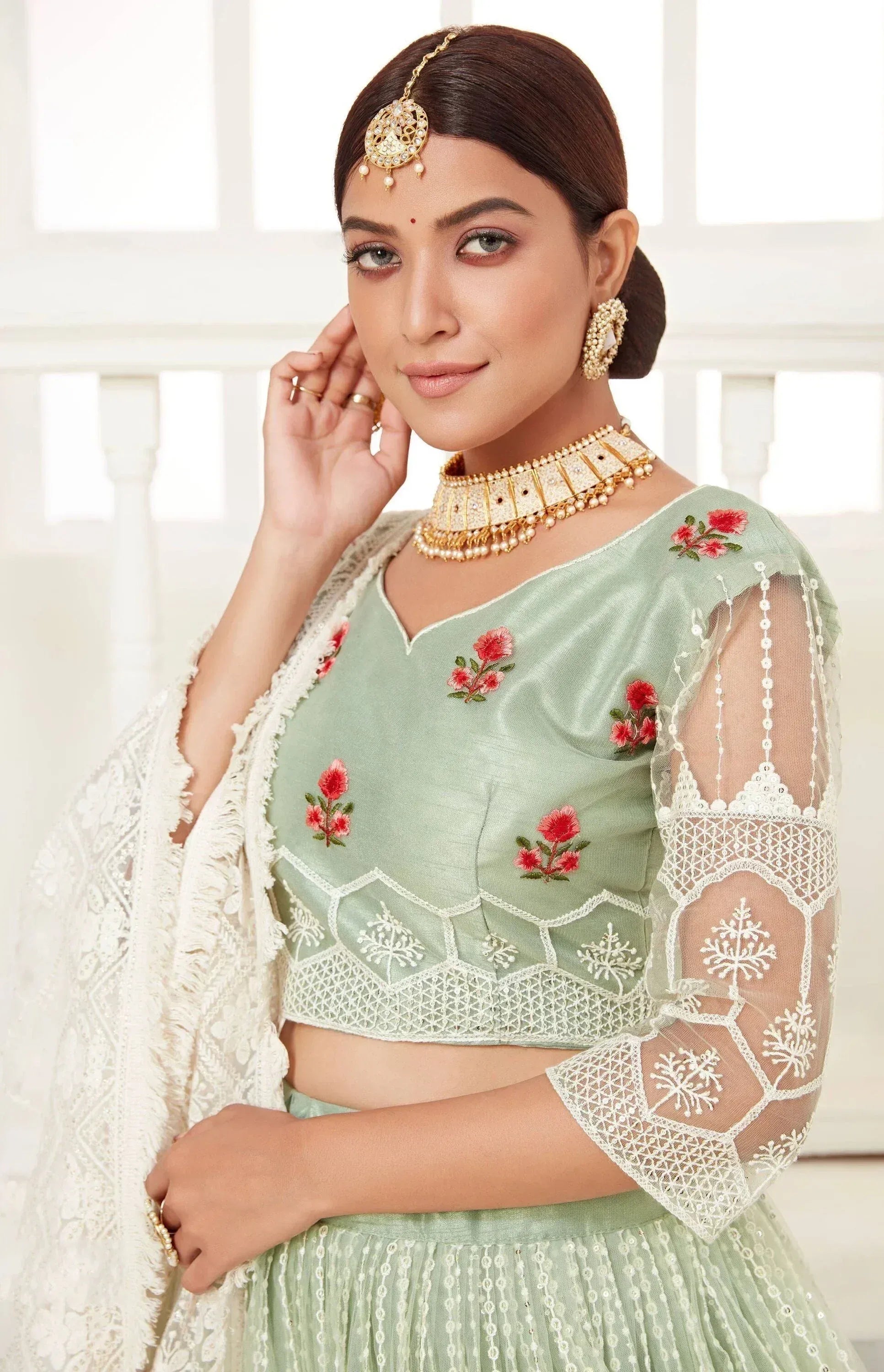 Mint green embroidered lehenga choli with floral motifs and lace sleeves, paired with gold jewelry