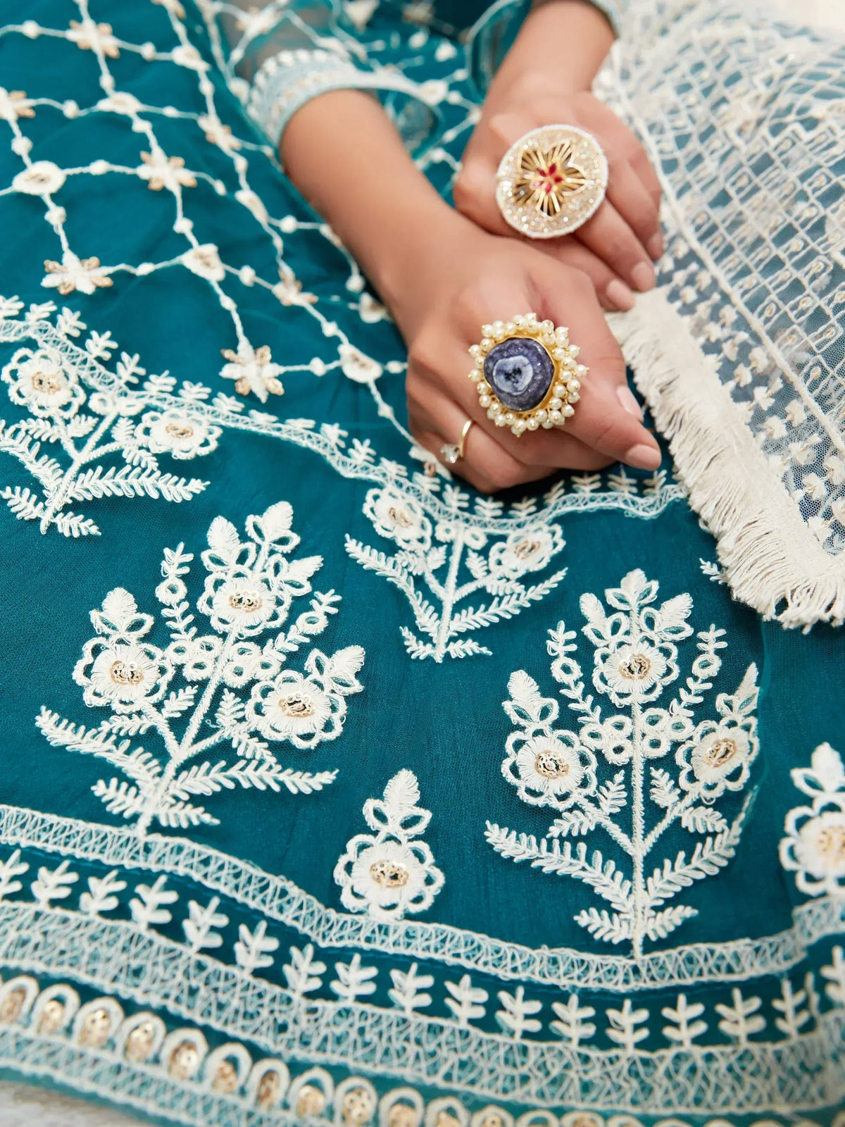 Teal ethnic gown with white floral embroidery and statement rings, perfect for Indian occasions