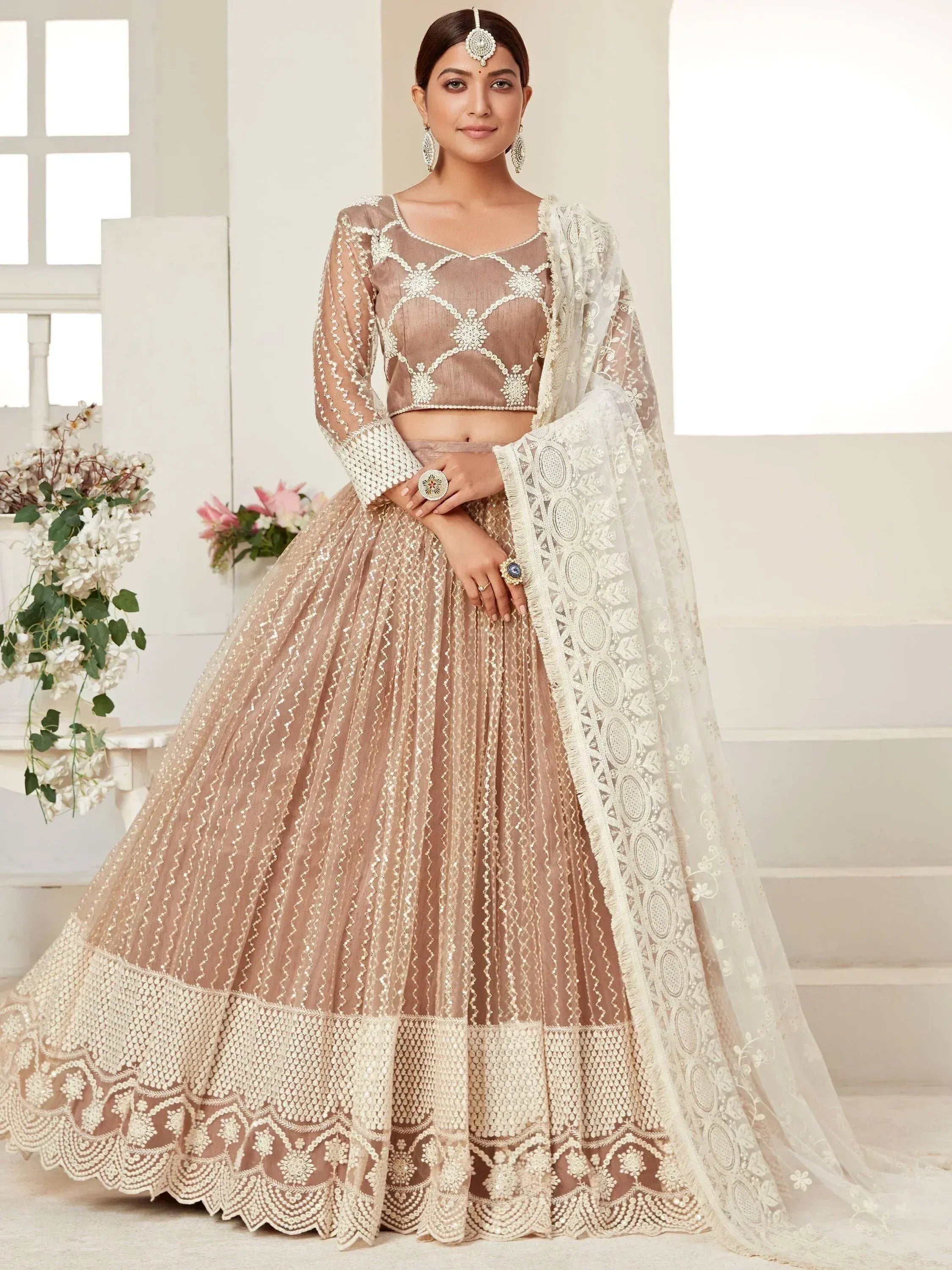 Elegant beige lehenga choli with intricate white embroidery and sheer dupatta, perfect for Indian weddings or festive occasions.