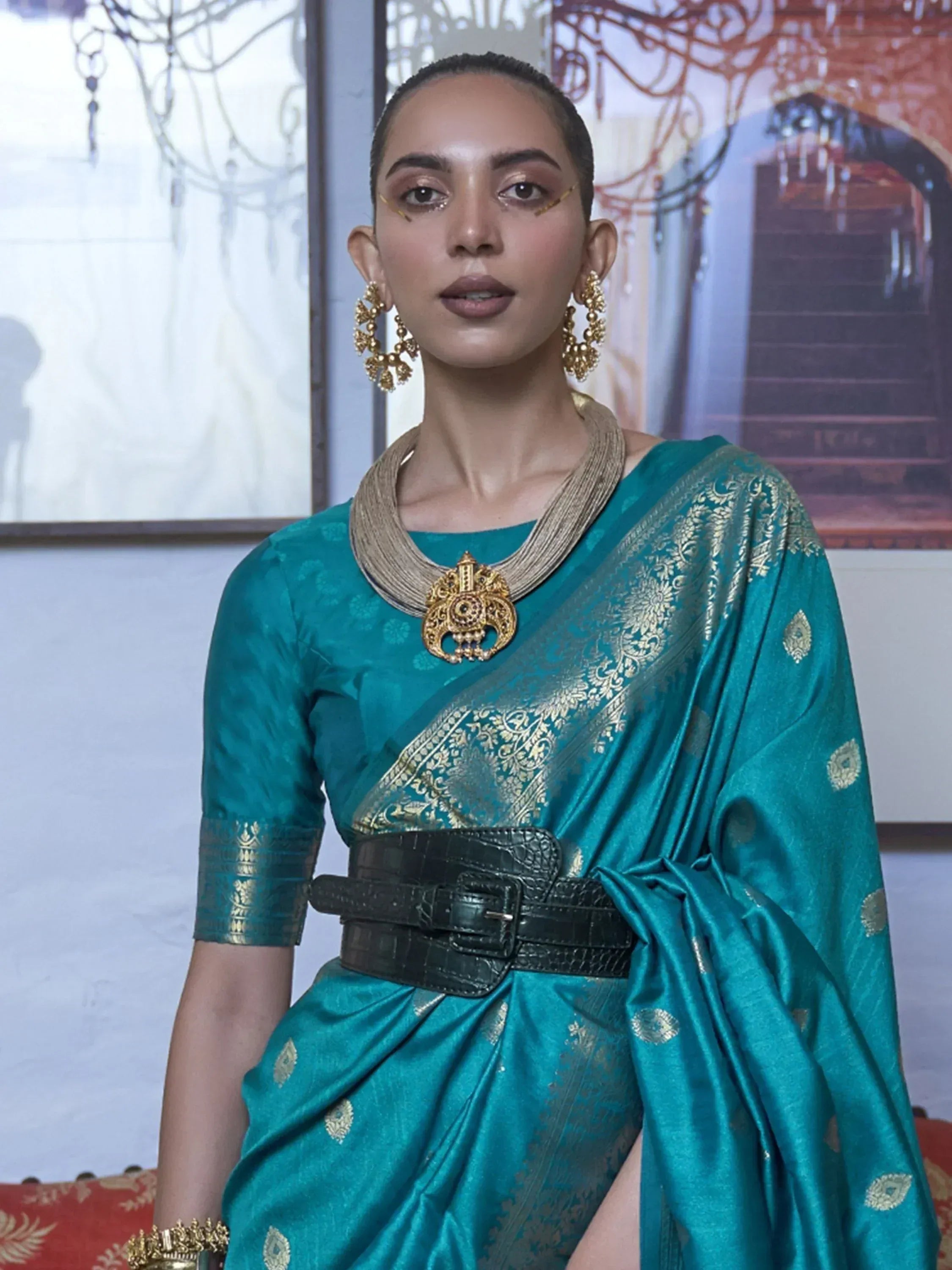 Teal silk saree with gold embroidery, statement necklace, and black belt for ethnic wear