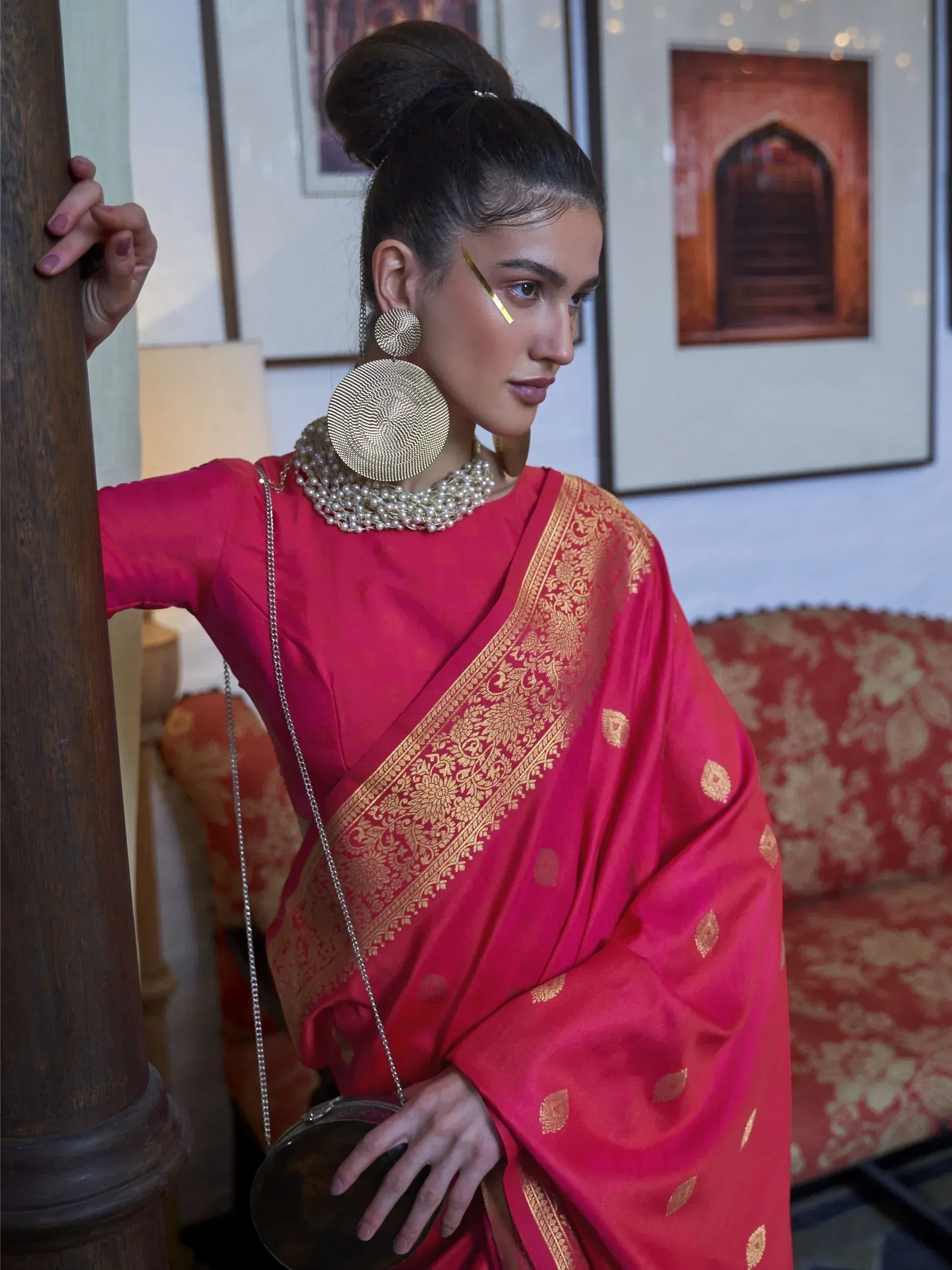Woman in vibrant red saree with gold embroidery, styled with statement earrings and pearl necklace for ethnic occasions