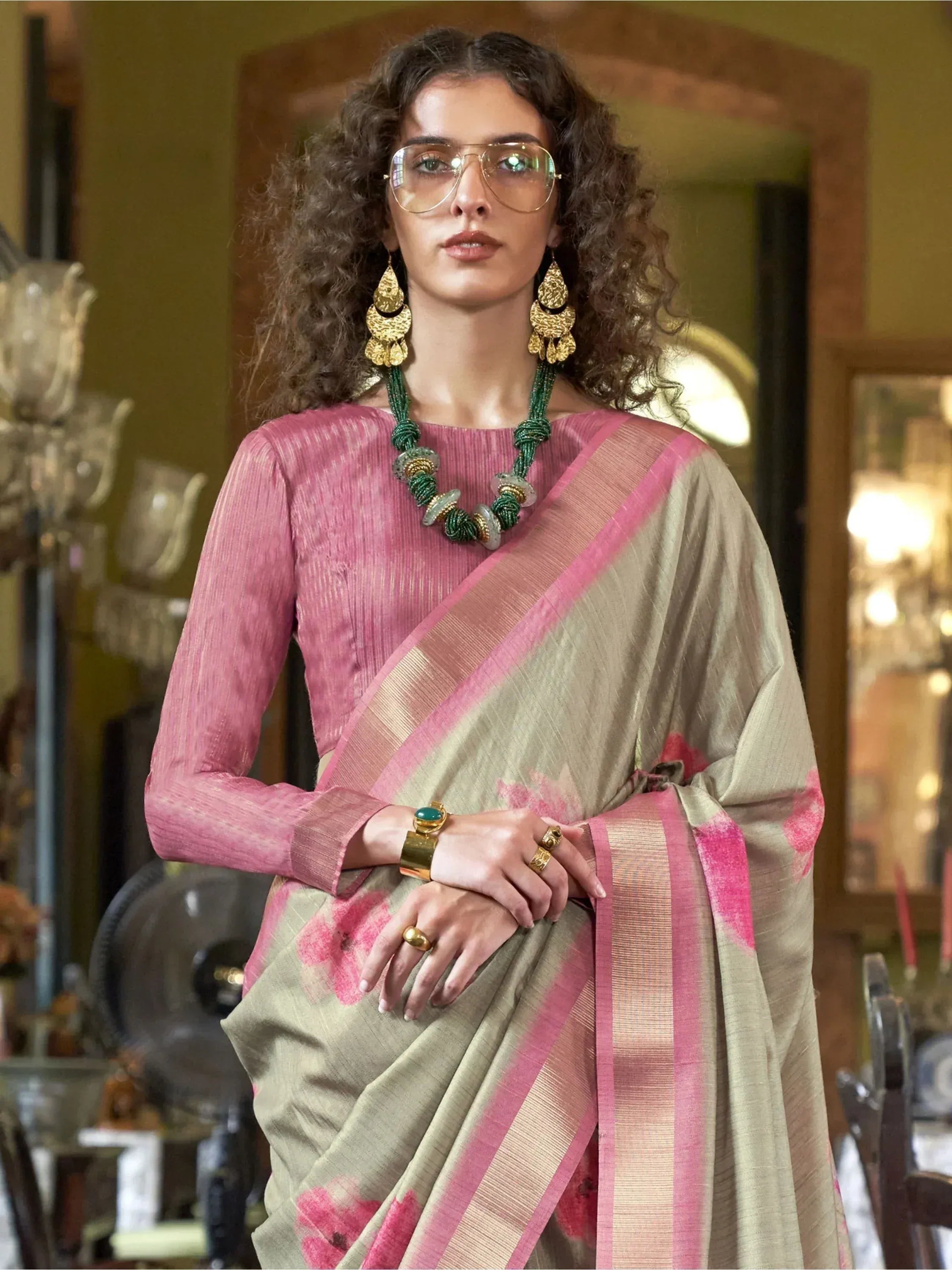 Woman in pink and beige saree with floral print, styled with gold jewelry and glasses