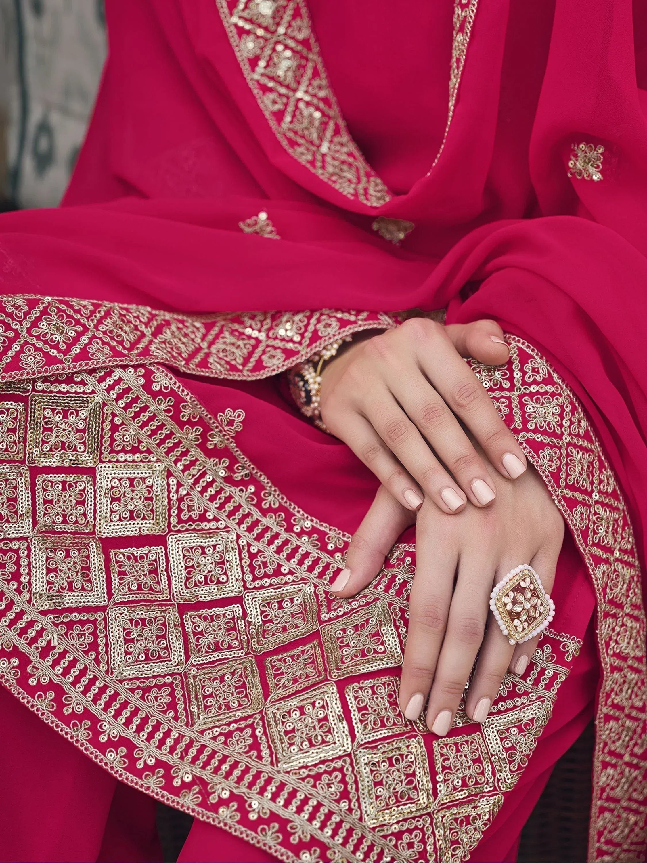 Close-up of hands resting on a pink embroidered saree with gold detailing and statement ring