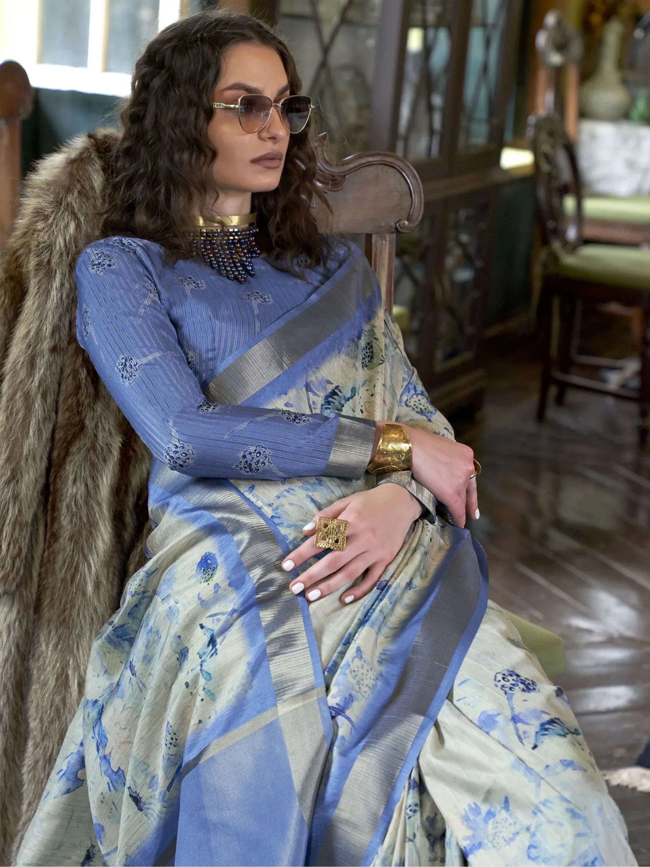Woman in blue floral saree with gold jewelry and fur stole, stylish ethnic wear