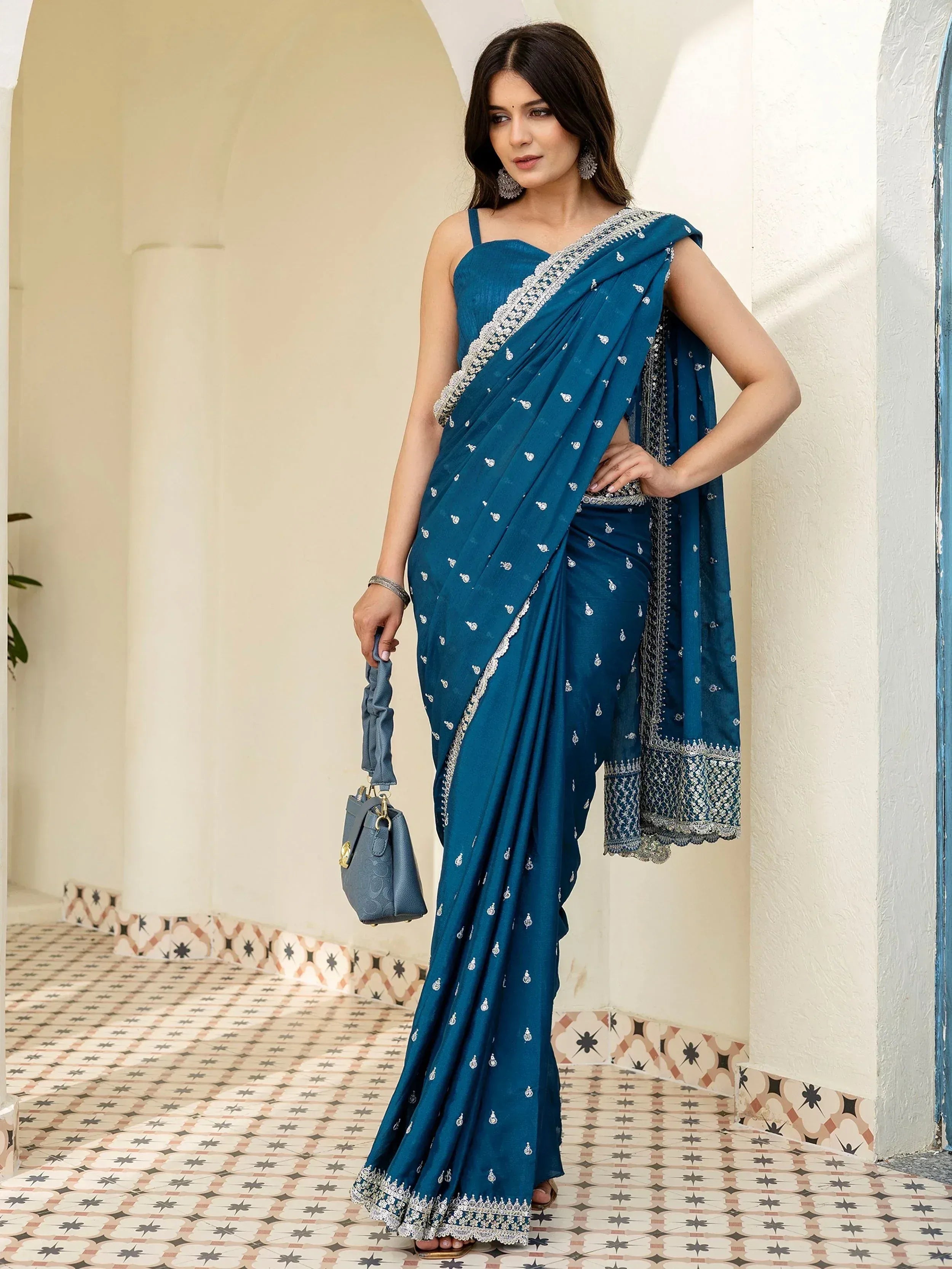 Elegant teal saree with silver embroidery, paired with matching blouse and handbag, perfect for Indian ethnic occasions.