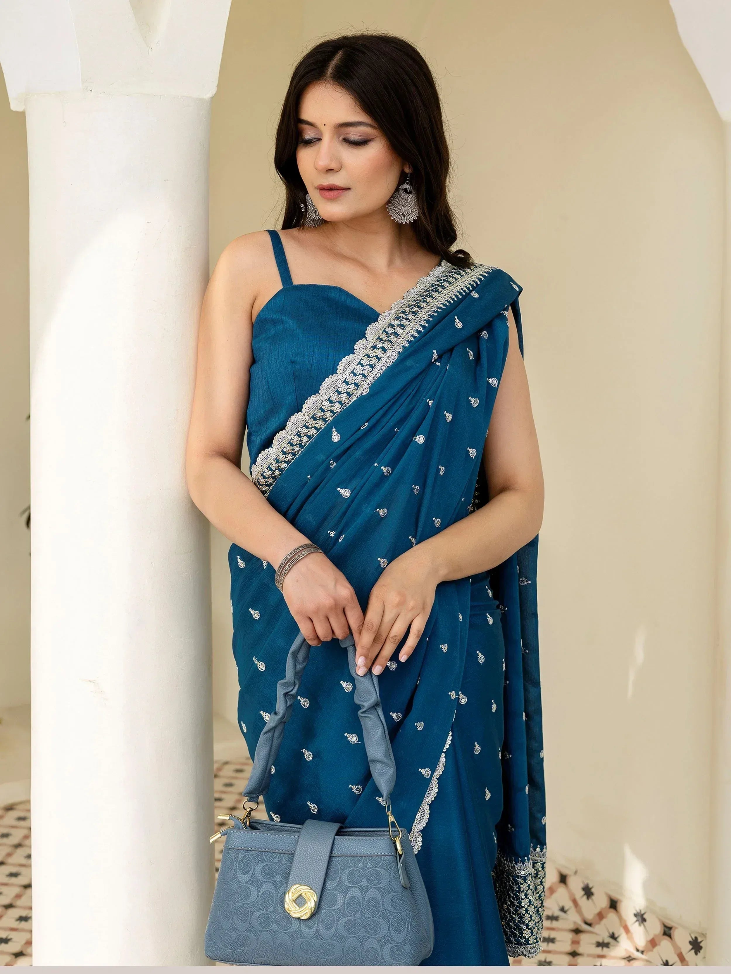 Blue embroidered saree with silver border, styled with statement earrings and a matching handbag for ethnic occasions.