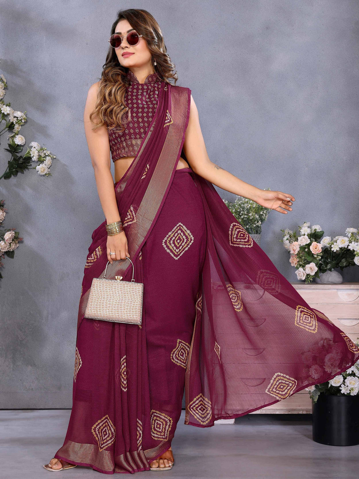 Maroon ethnic saree with gold geometric print, sleeveless blouse, and matching clutch for Indian occasions