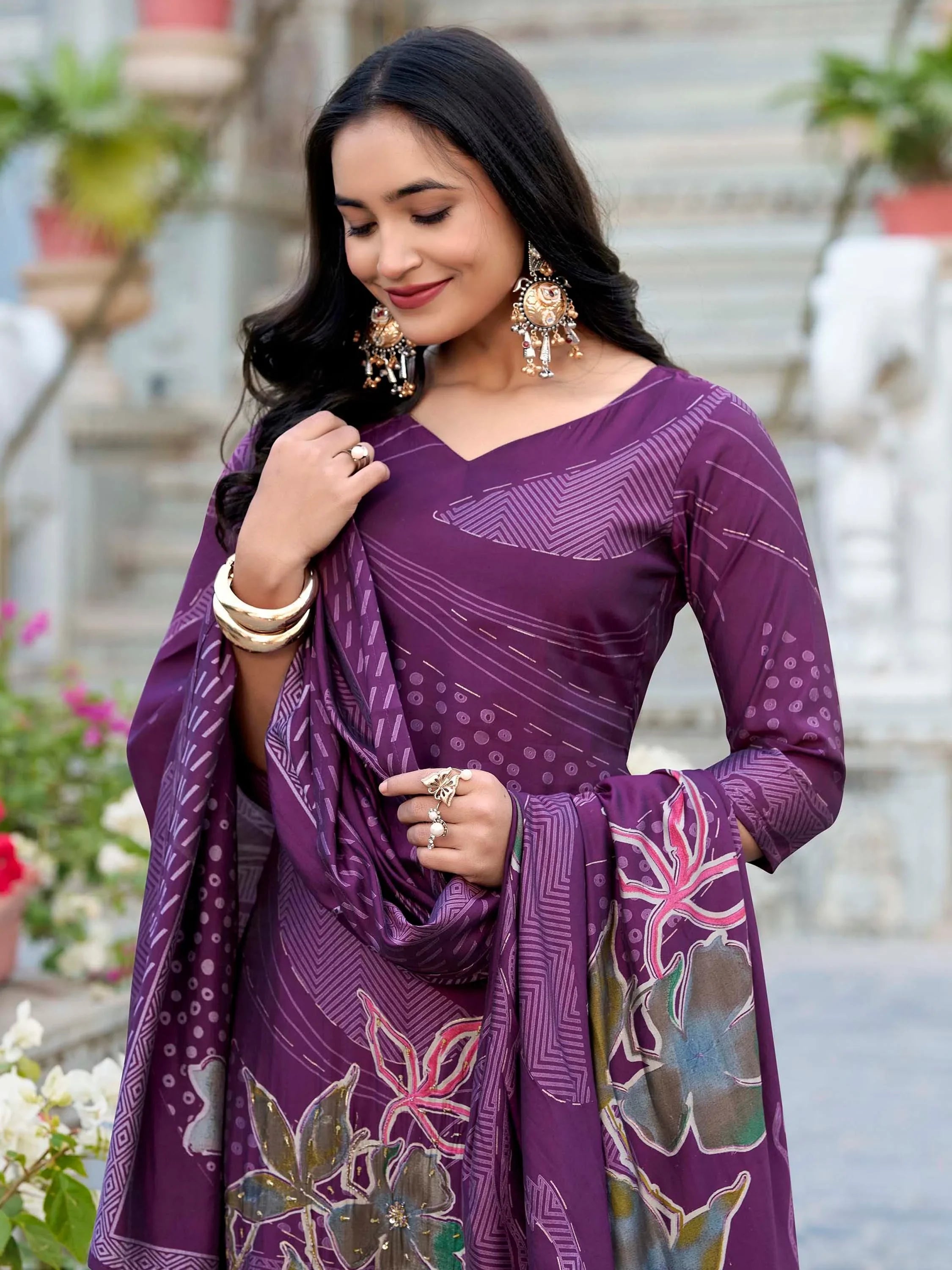 Woman in a purple printed ethnic salwar kameez with floral dupatta and gold jewelry