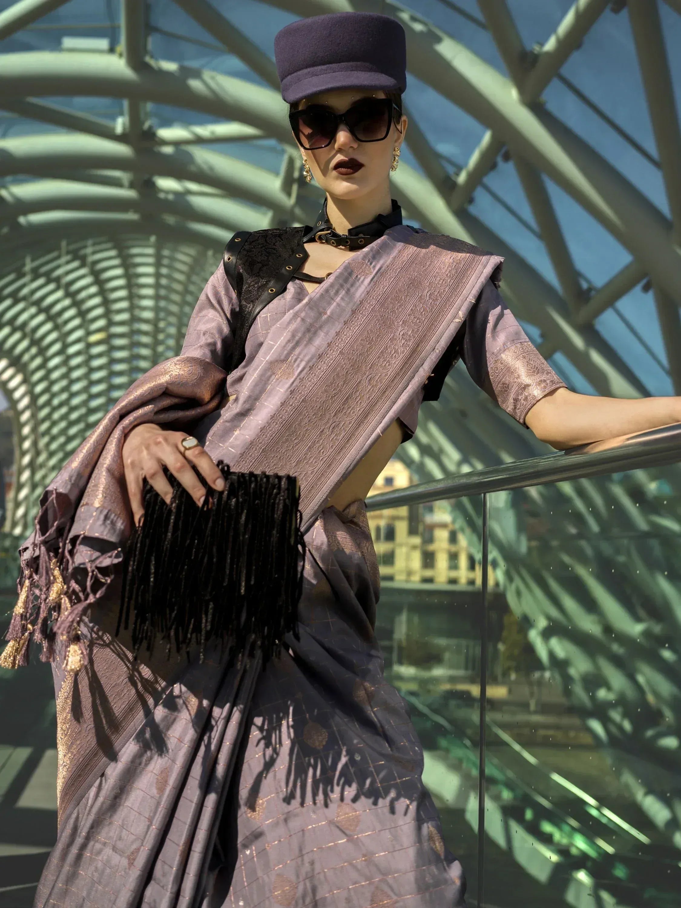 Stylish purple saree with gold motifs, black leather accents, and fringe clutch, paired with a cap and sunglasses.