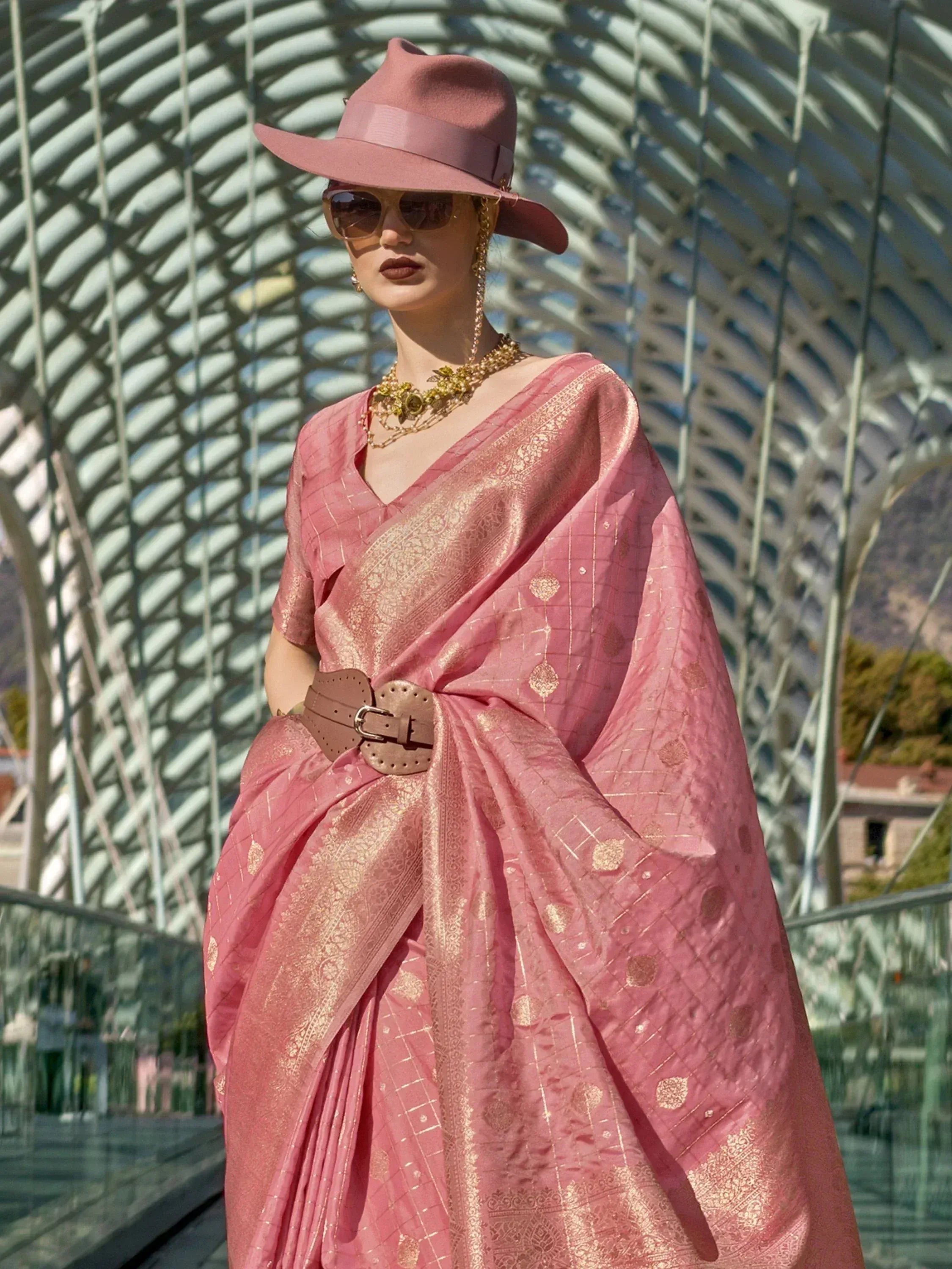 Pink designer saree with gold motifs, styled with hat and belt for ethnic fashion