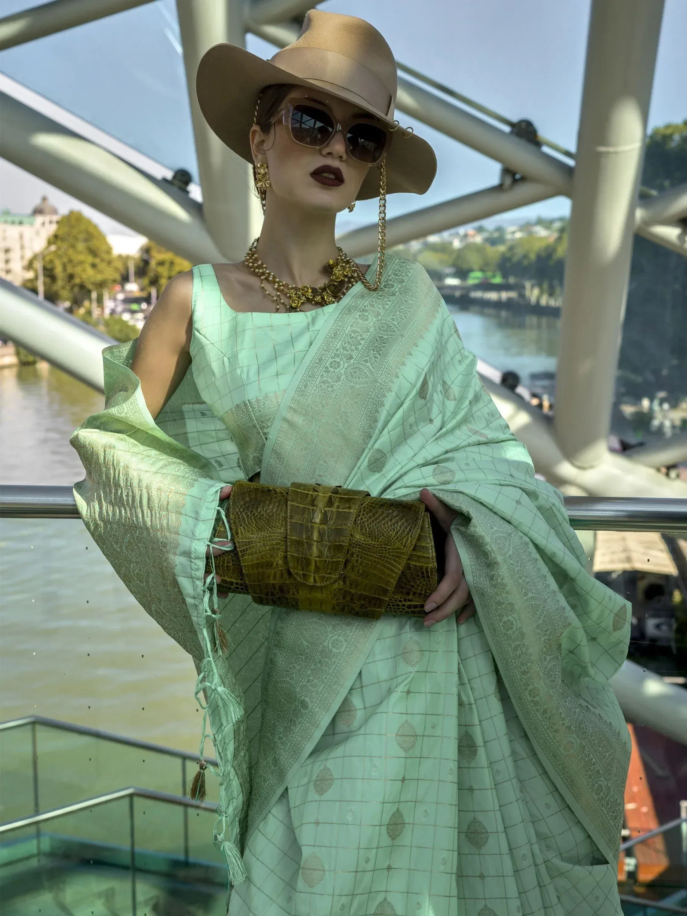 Mint green designer saree with gold embroidery, paired with wide-brim hat and statement jewelry for ethnic fashion.